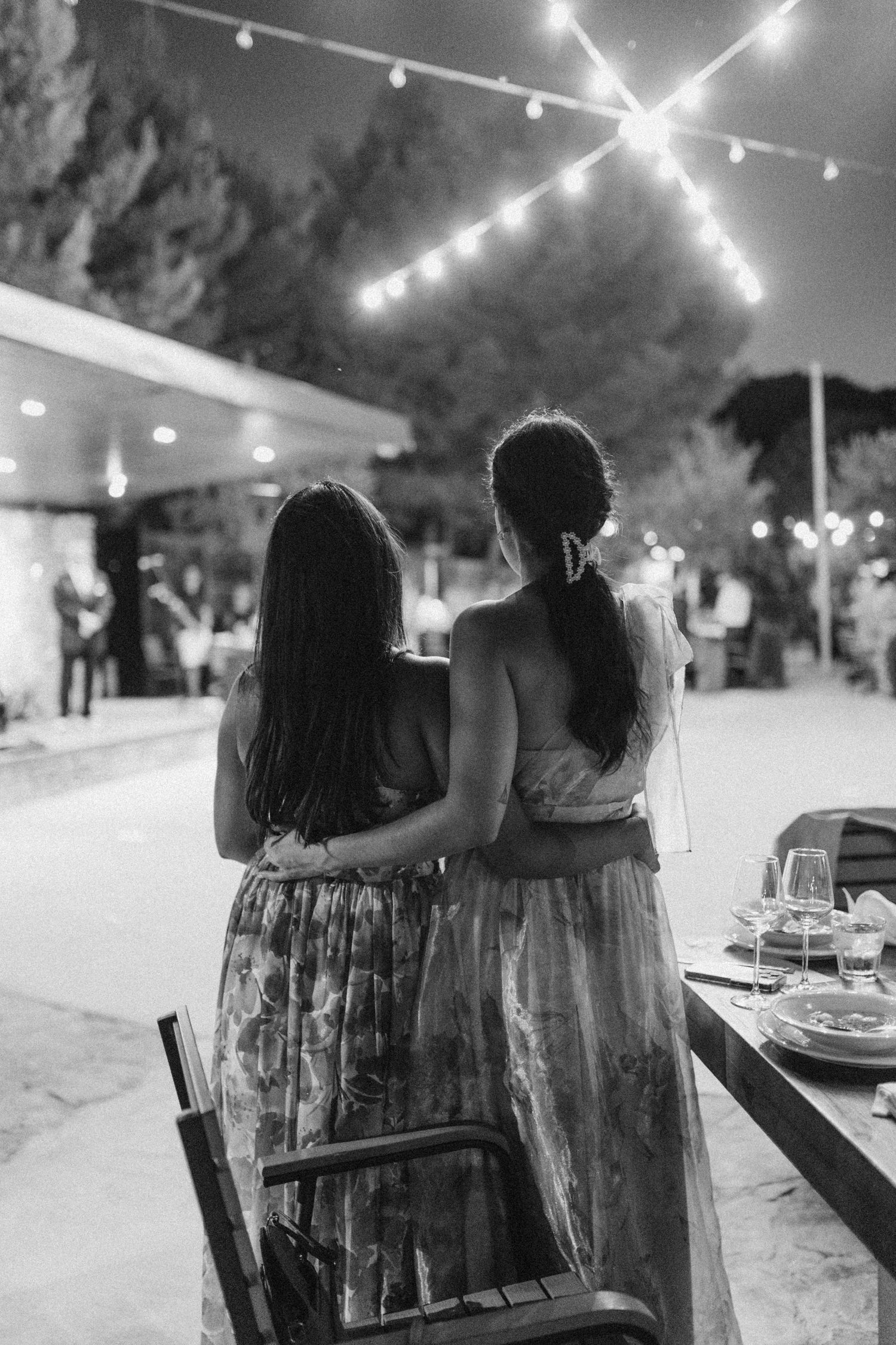 Wedding guests sit together under string lights during an evening outdoor reception.