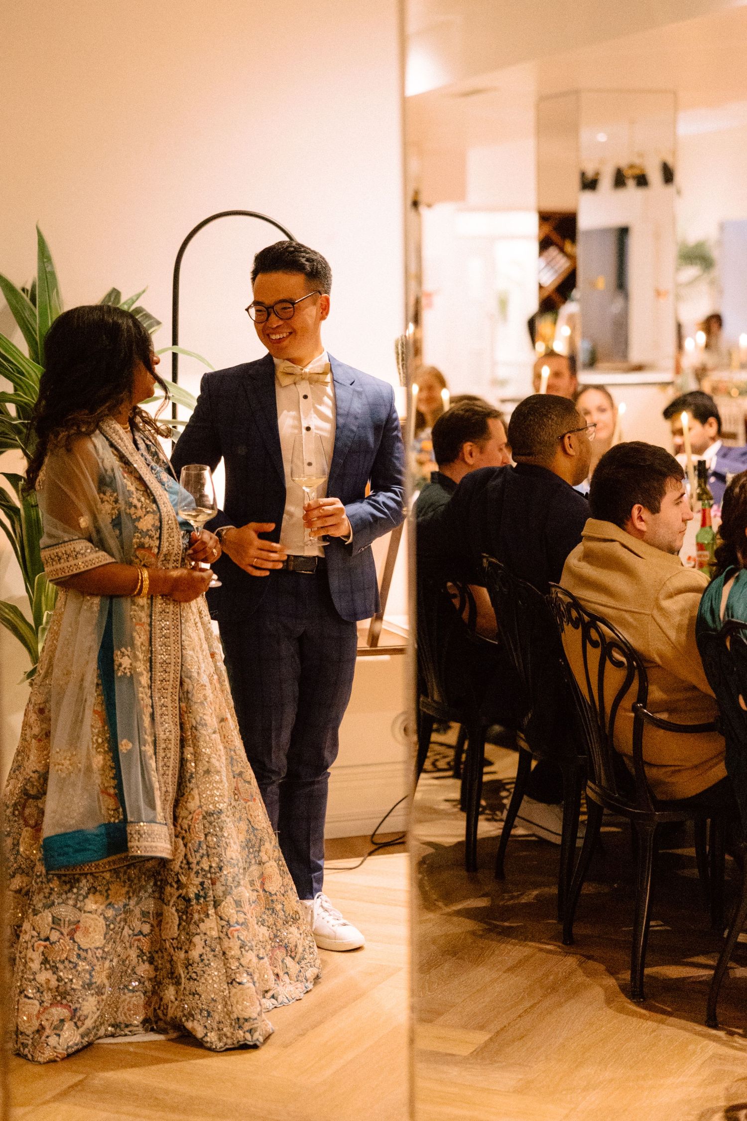 Man in blue suit chats with woman in floral lehenga at elegant indoor wedding reception.