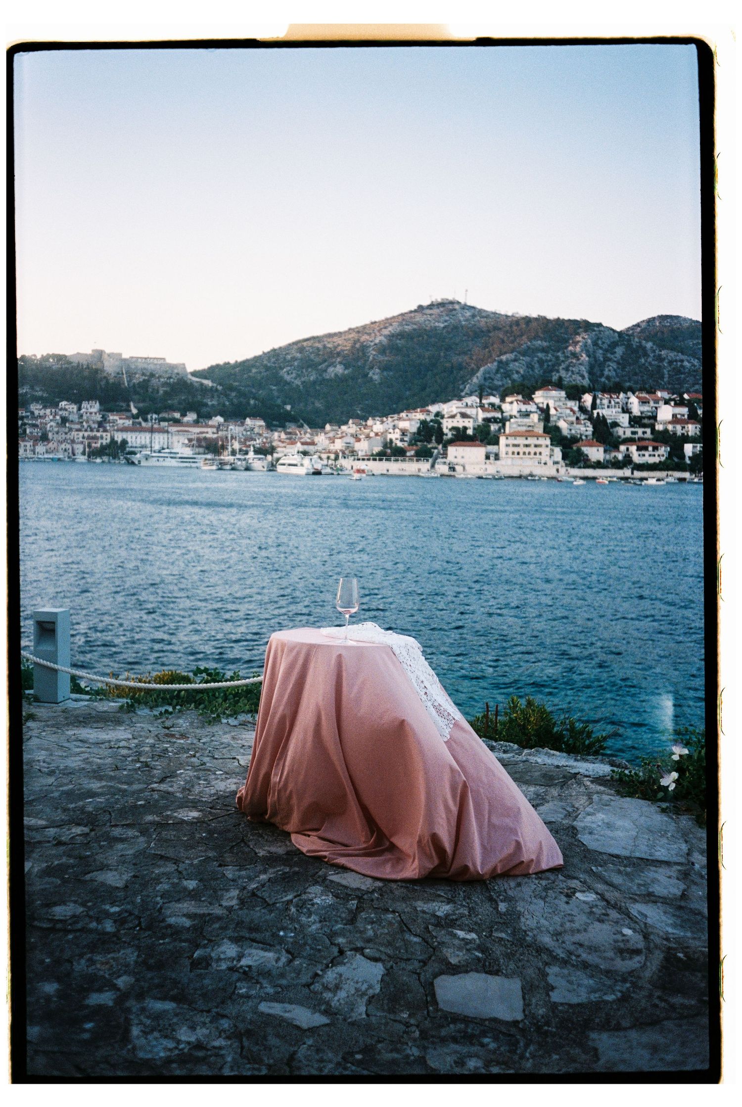 Pink draped table overlooks stunning Mediterranean coastal town at dusk.