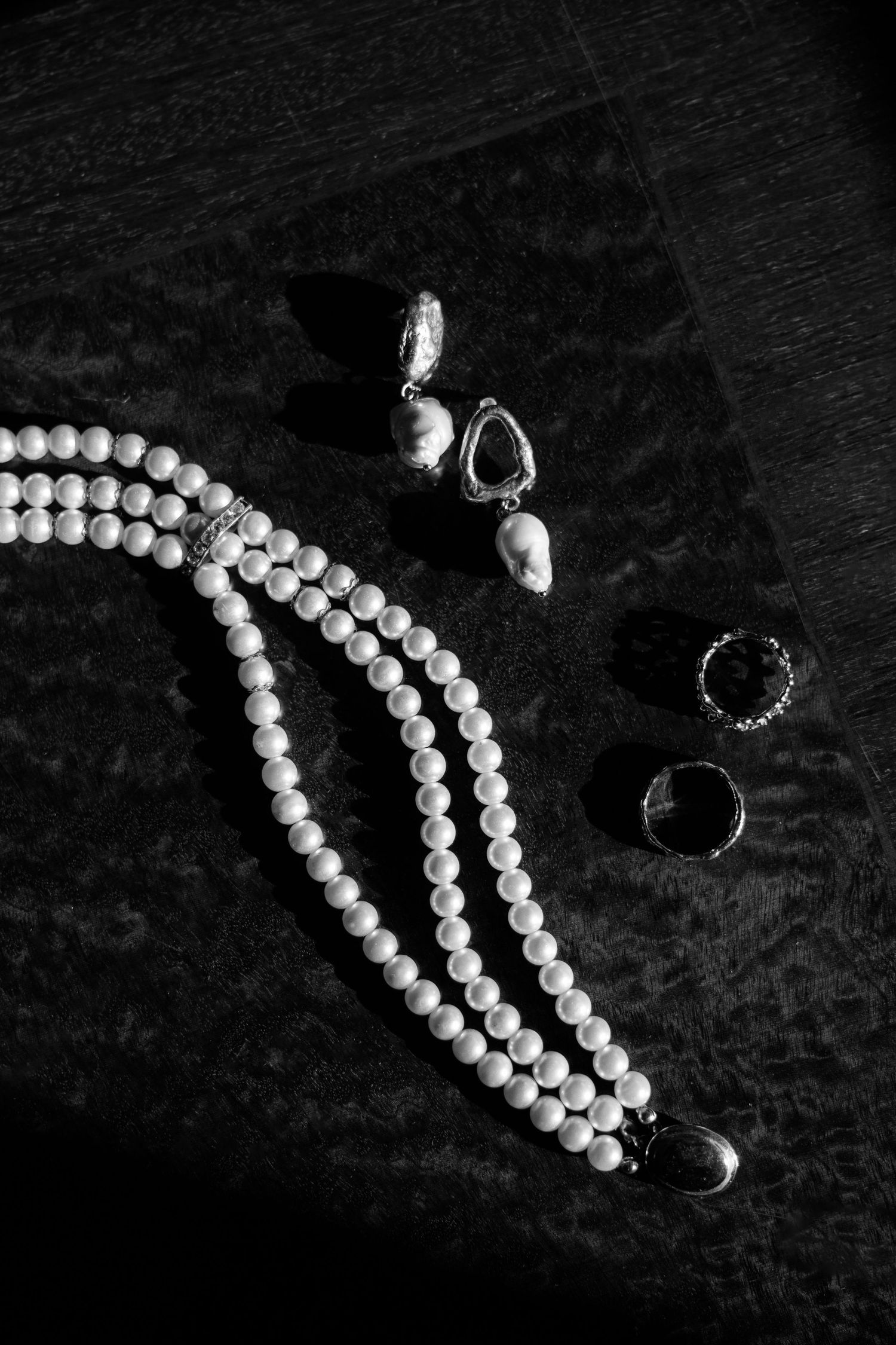 Pearl necklace and jewelry pieces arranged on dark textured background in black and white.
