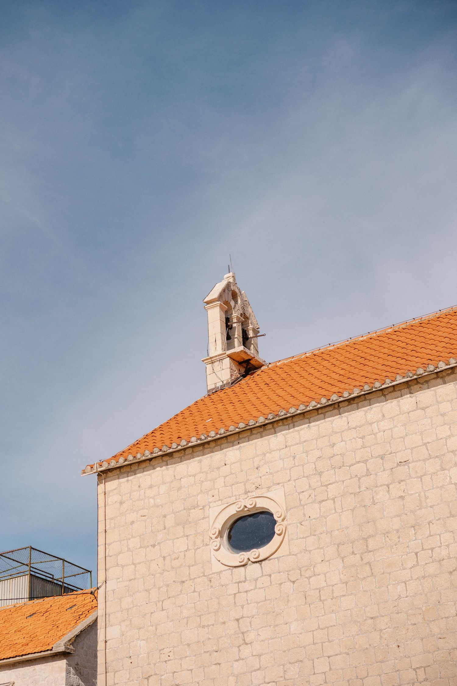Orange tiled roof and white stone church facade against blue sky.