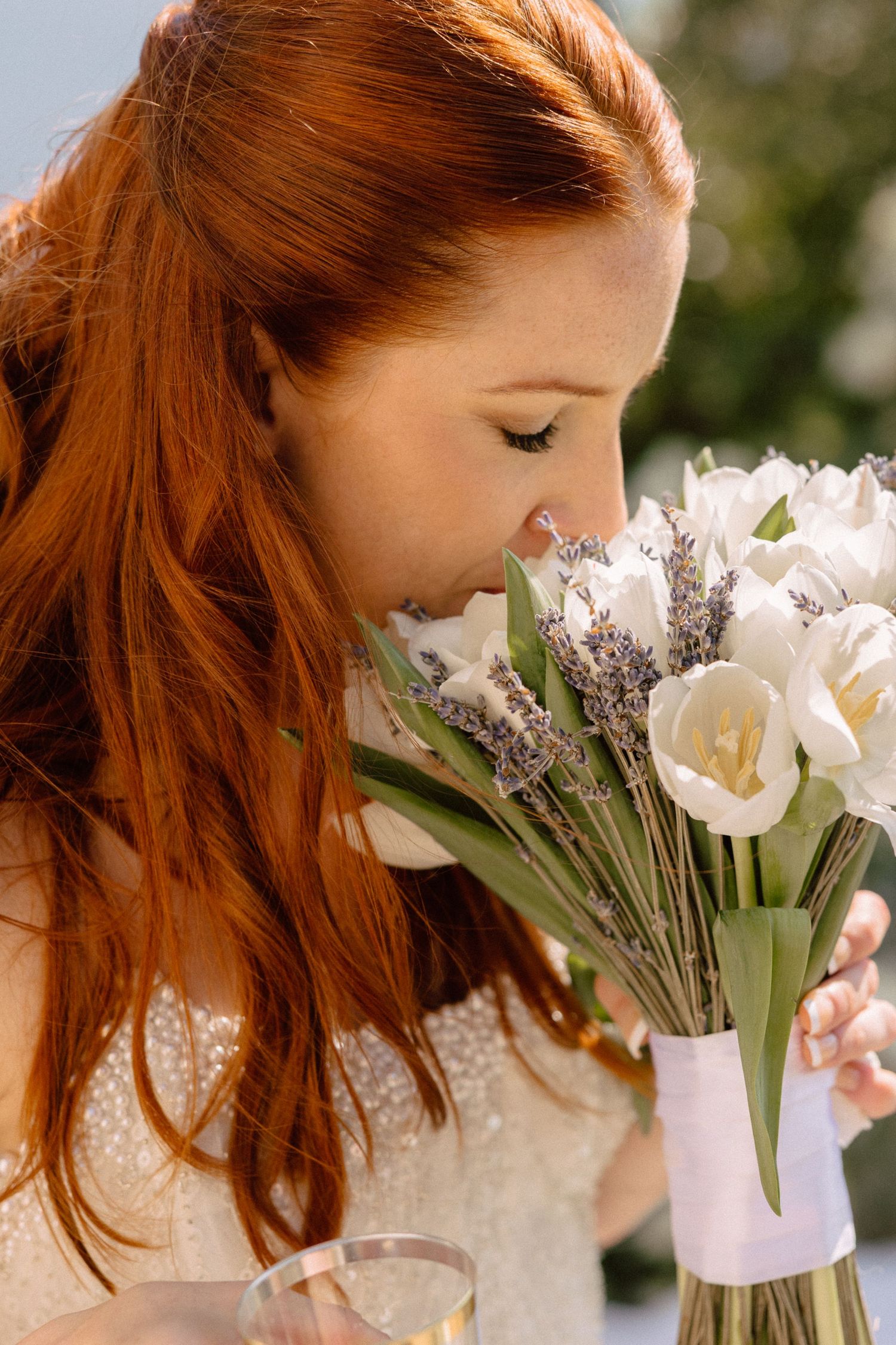 A delicate white and lavender bridal bouquet being held in natural sunlight.