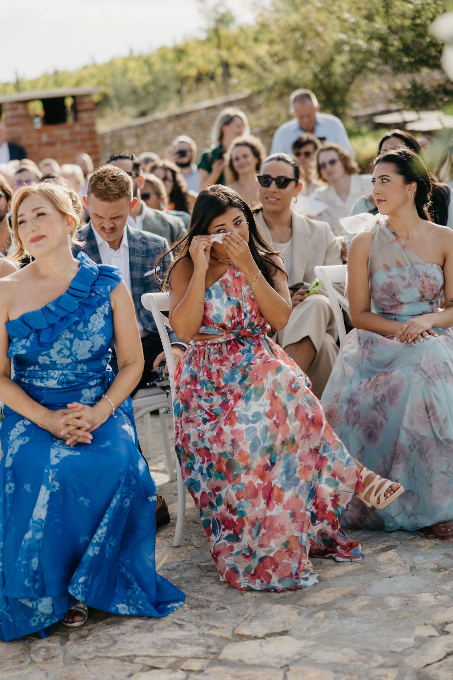 Wedding party members in blue and floral dresses sitting together outdoors.