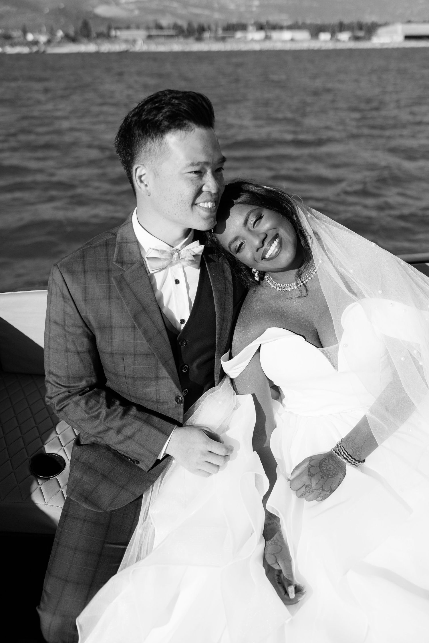 Black and white photo of joyful interracial newlyweds embracing on a boat by the water.