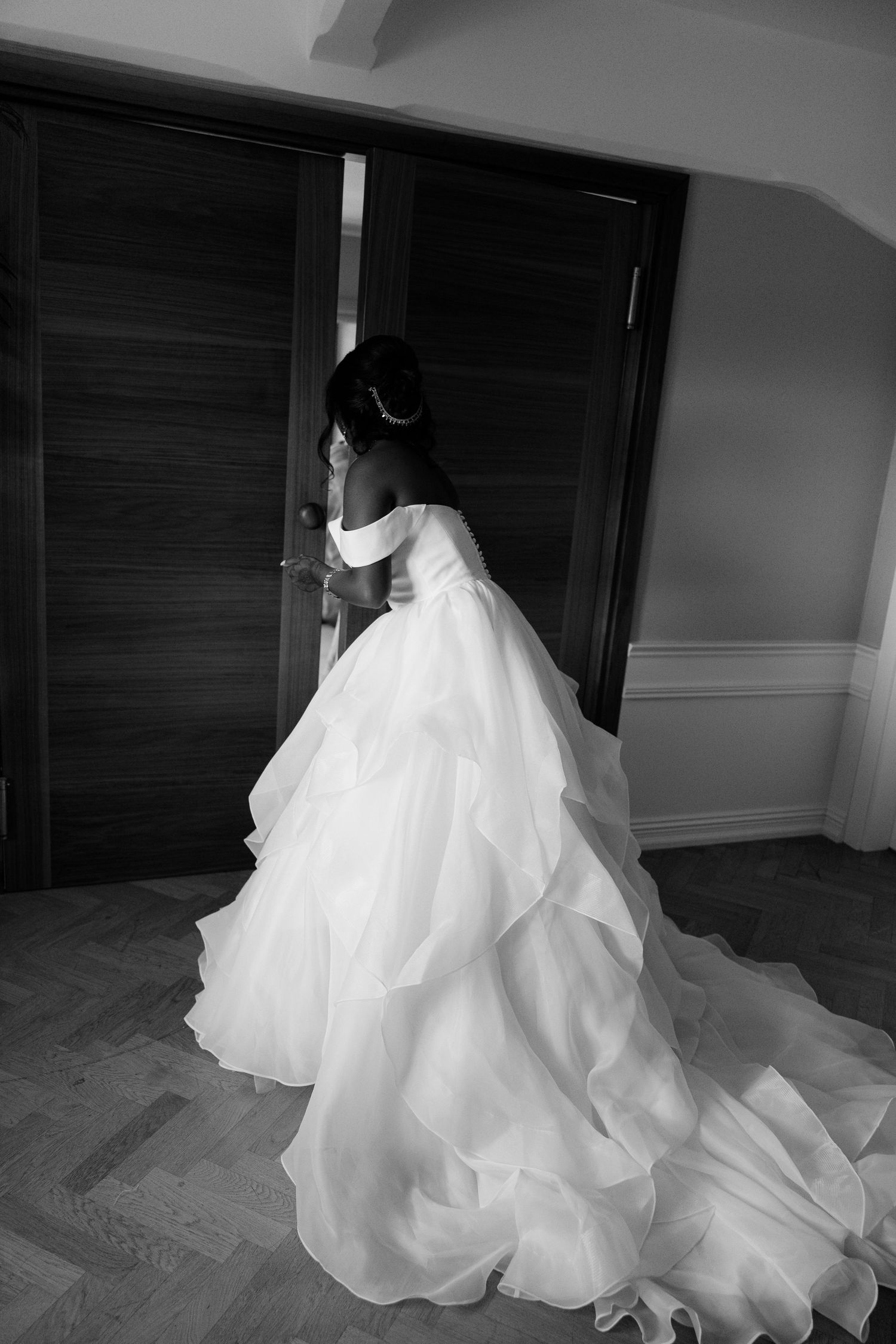 Bride in stunning layered ballgown wedding dress with long train standing by wooden doors.