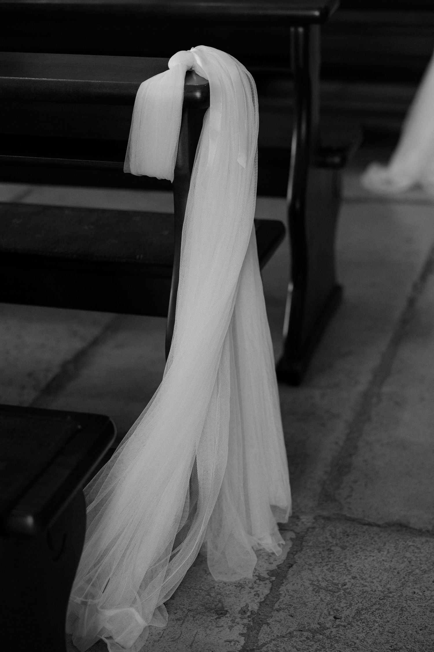 A flowing white wedding veil draped elegantly over a wooden church pew in black and white.