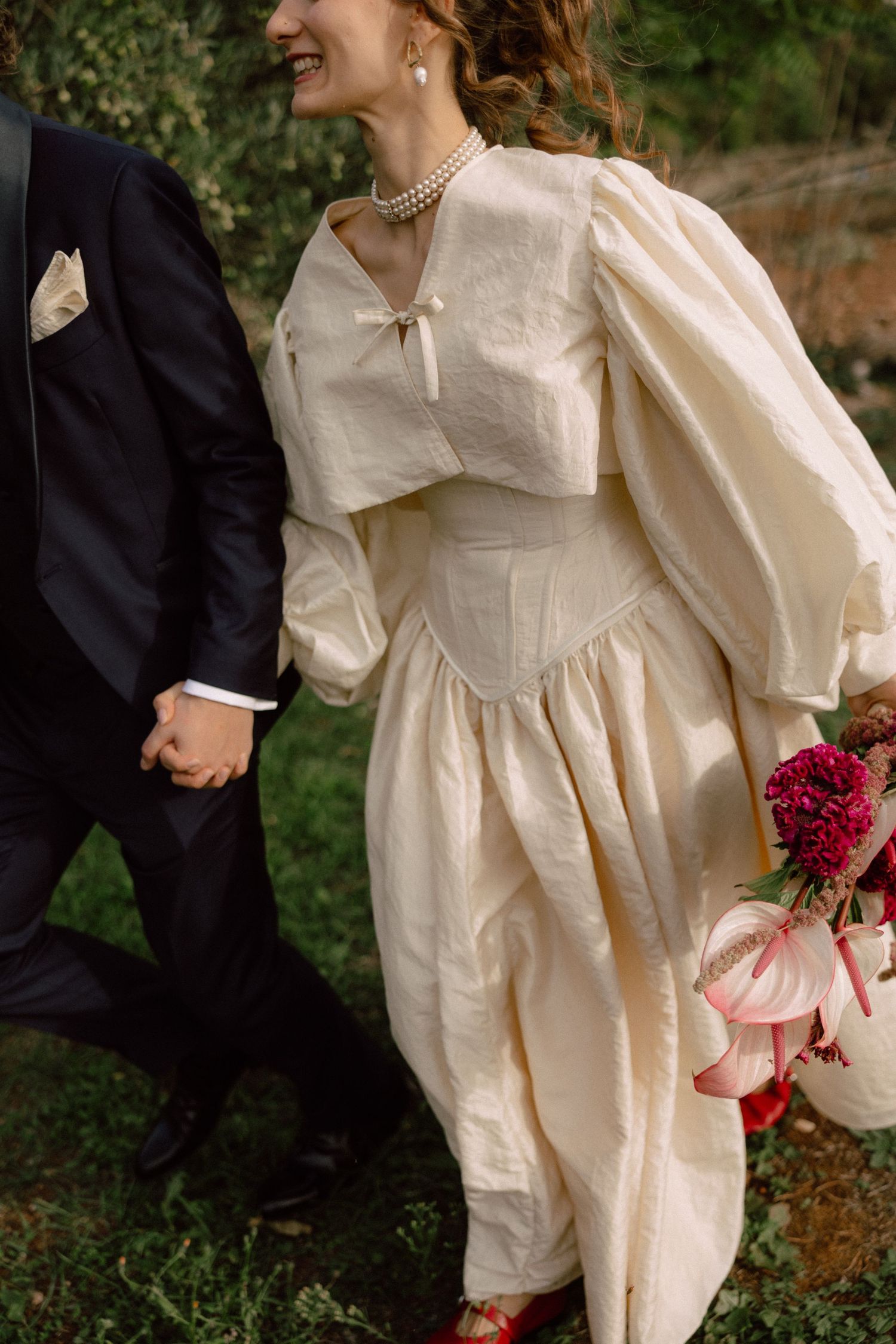 Bride in vintage-style dress with puff sleeves holding red bouquet.