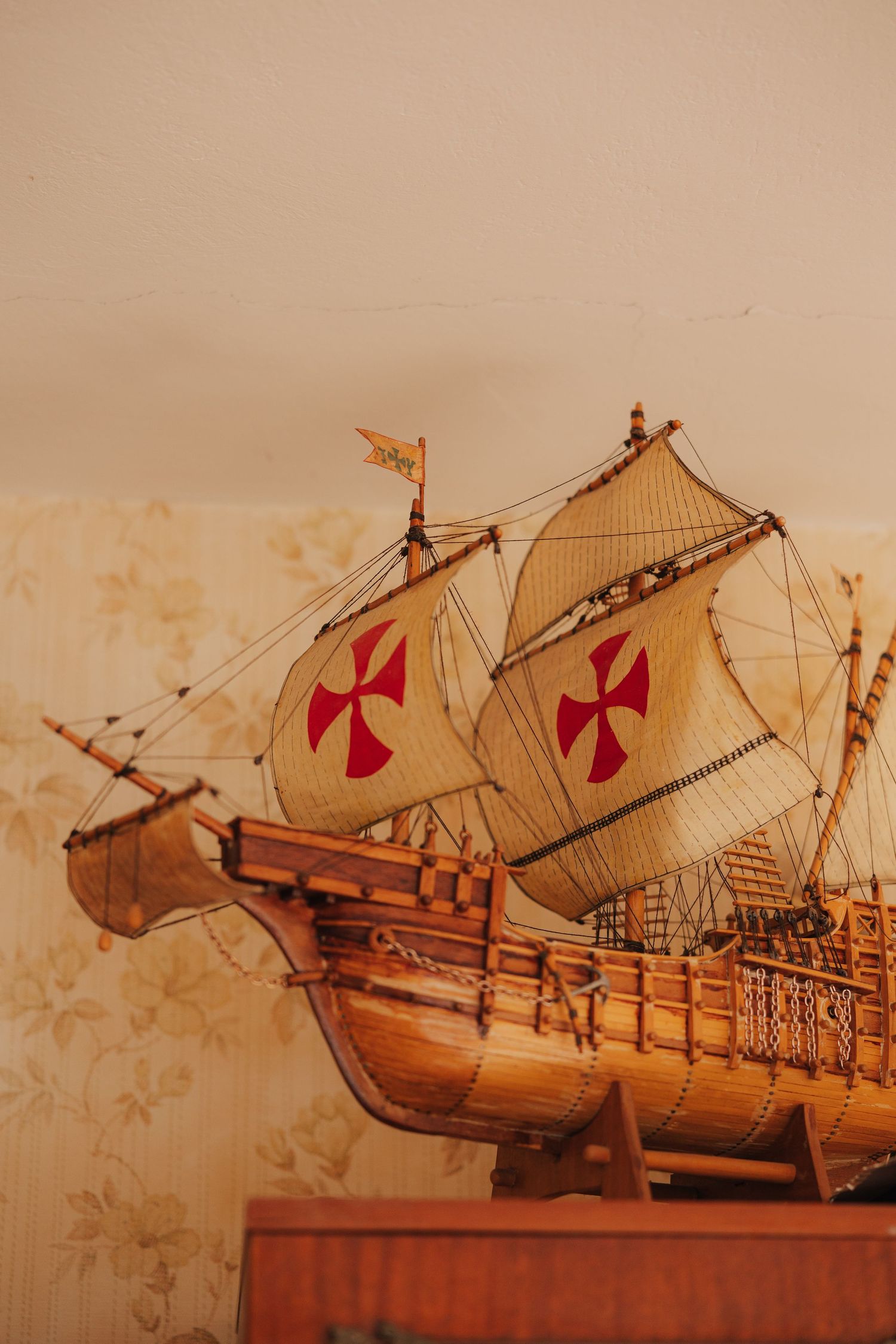 Vintage model ship with red cross sails displayed against sepia background.