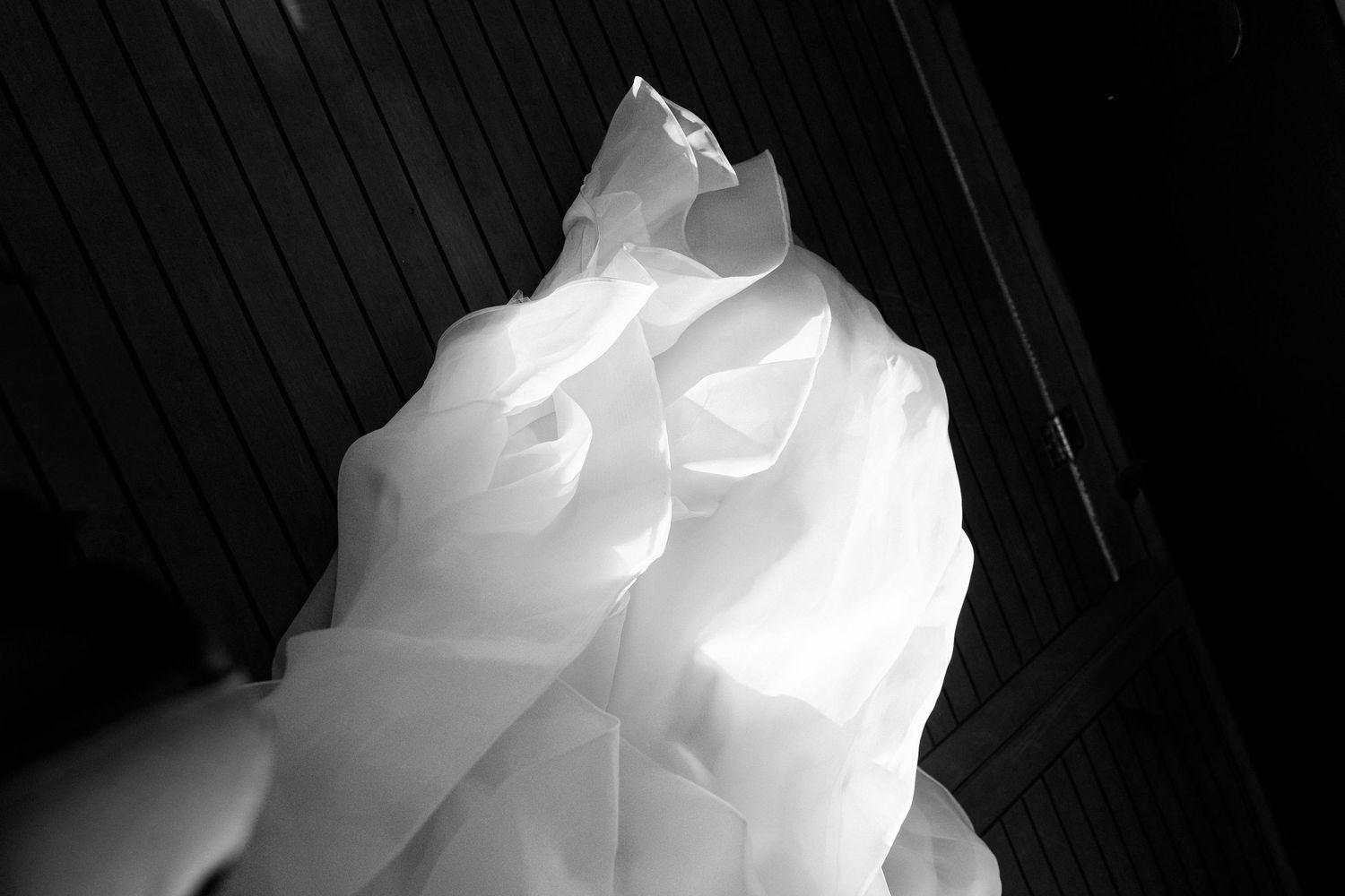 Black and white close-up of voluminous white wedding dress fabric with dramatic folds against dark background.