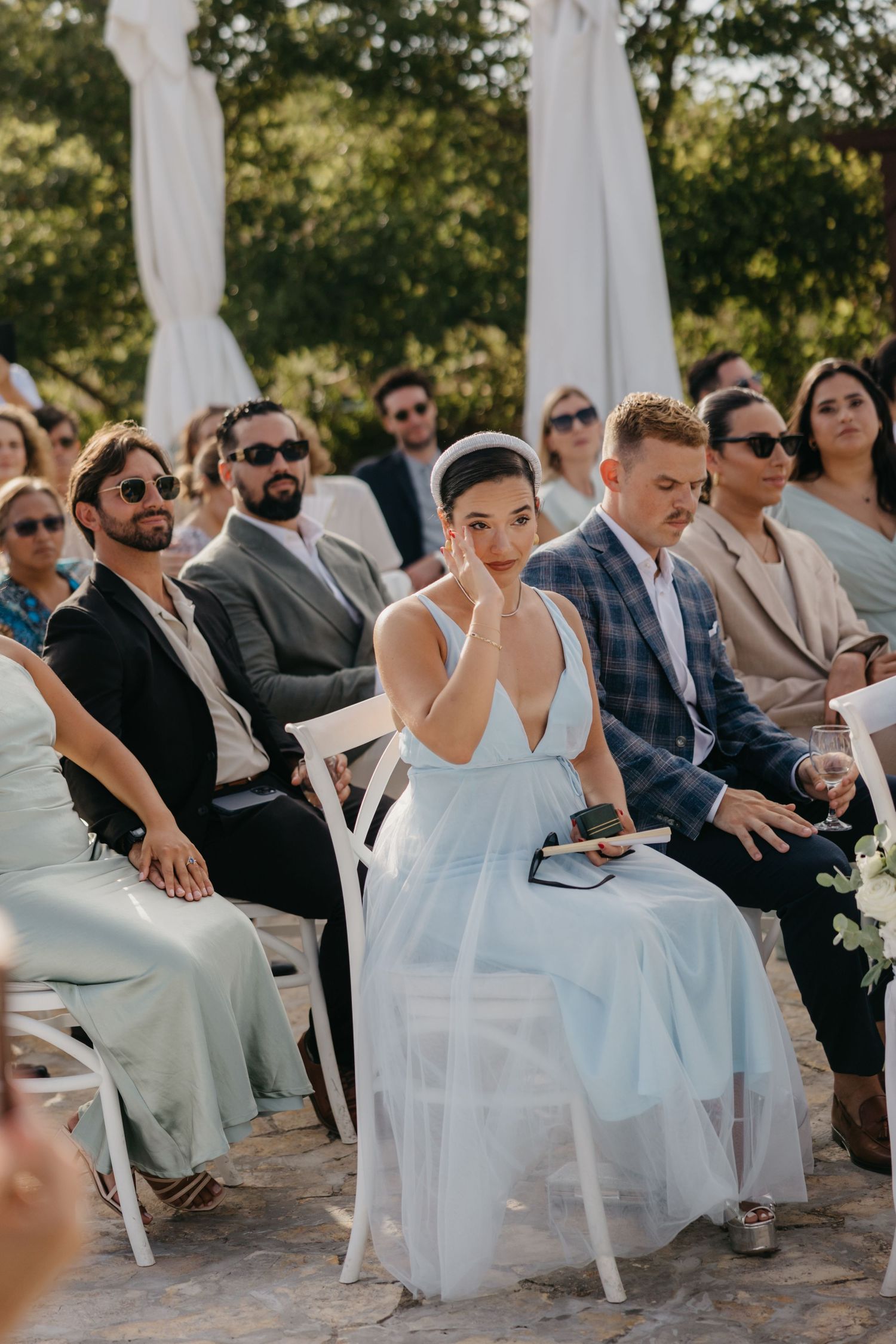 Wedding guests seated in white chairs during an outdoor ceremony.