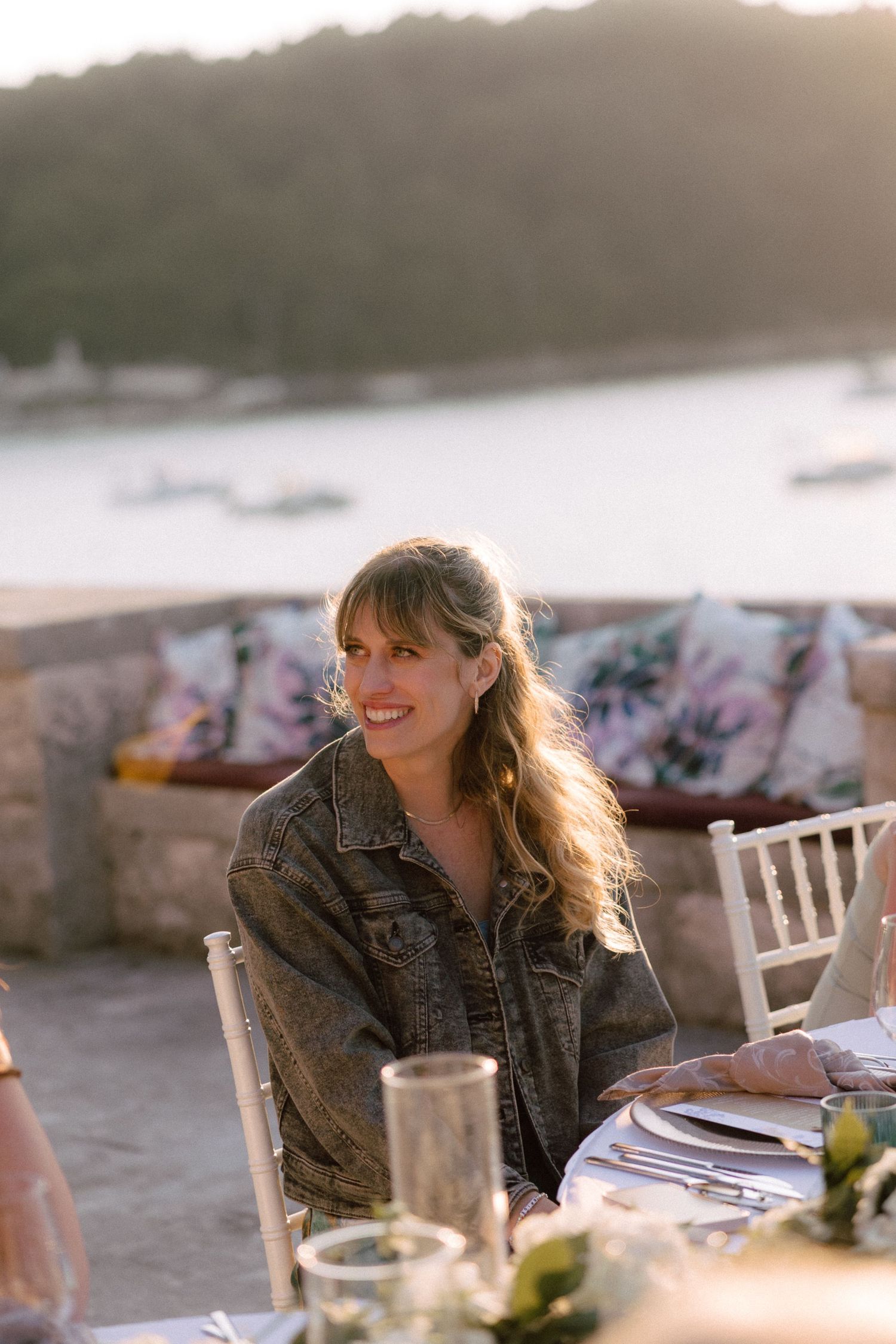 Golden hour outdoor dining setup with white chairs and coastal backdrop.