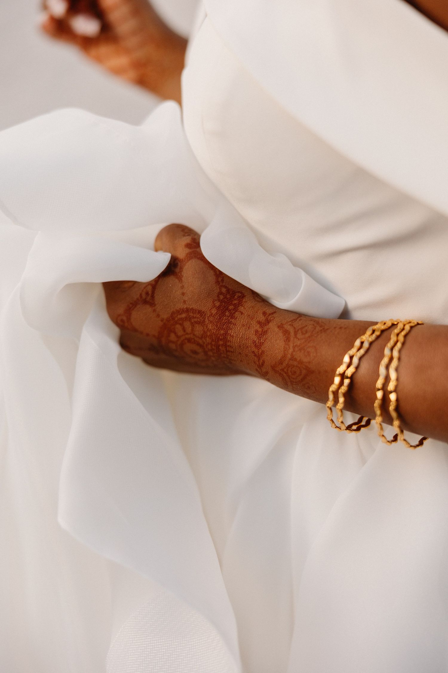 Bride in white wedding gown with intricate henna mehndi design and gold bracelets on her wrist.