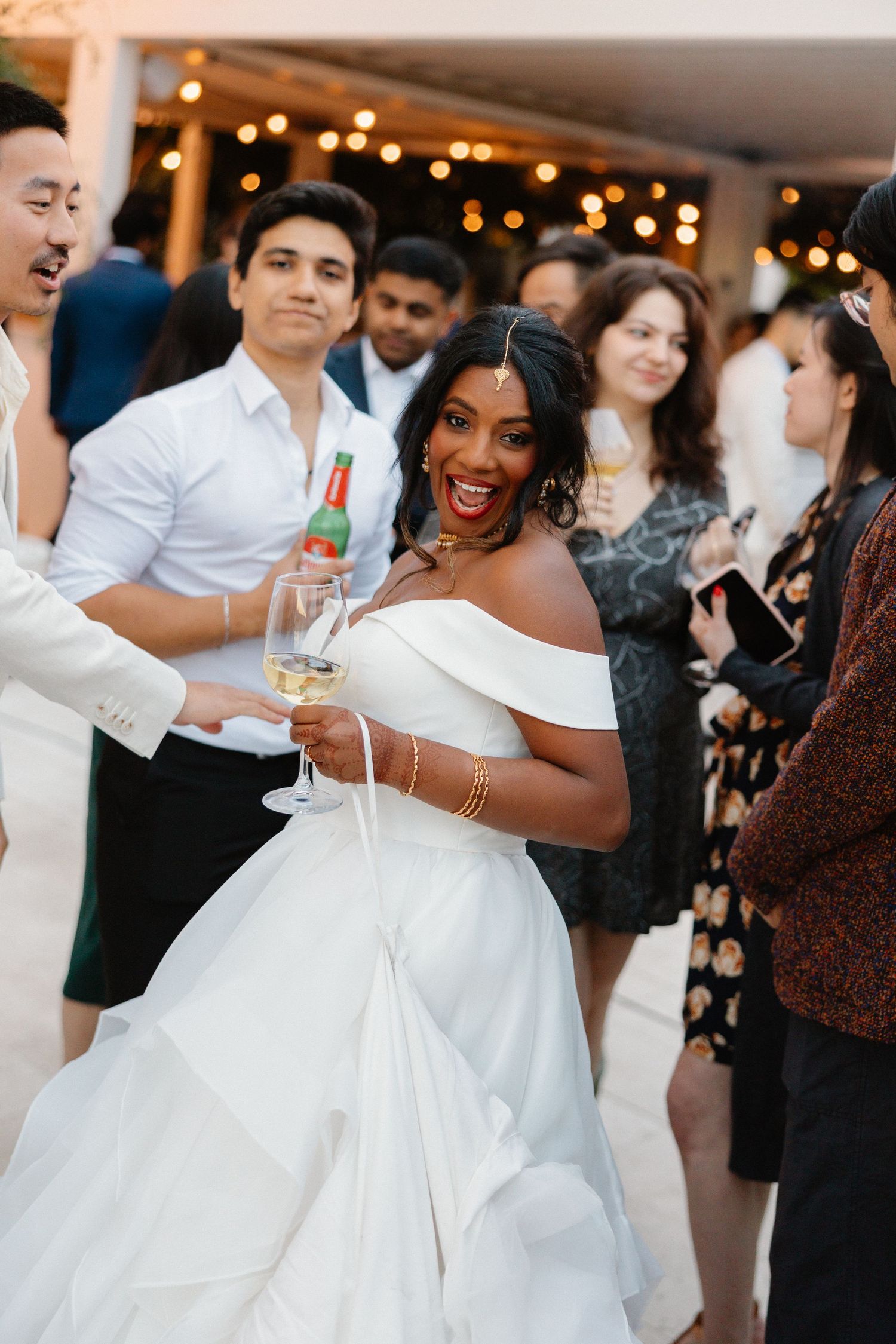 Radiant Black bride in off-shoulder white gown holding champagne glass celebrating at wedding reception.