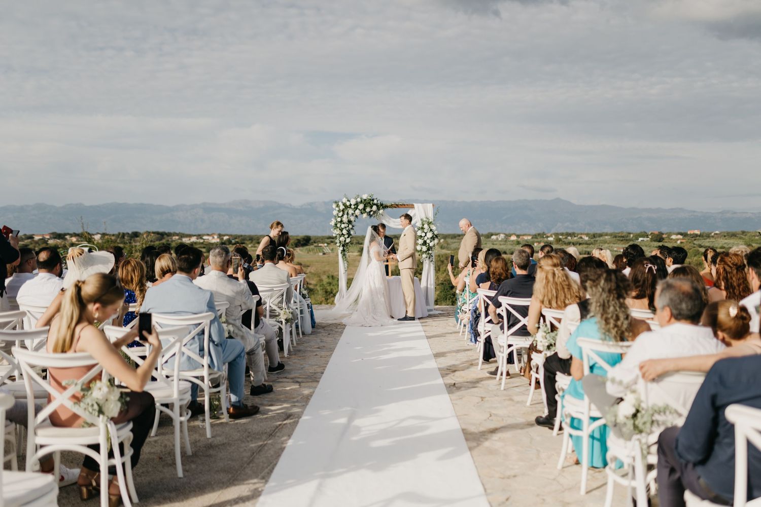 Rows of white chairs set up for an outdoor wedding ceremony with scenic ocean views in the background in Italy.