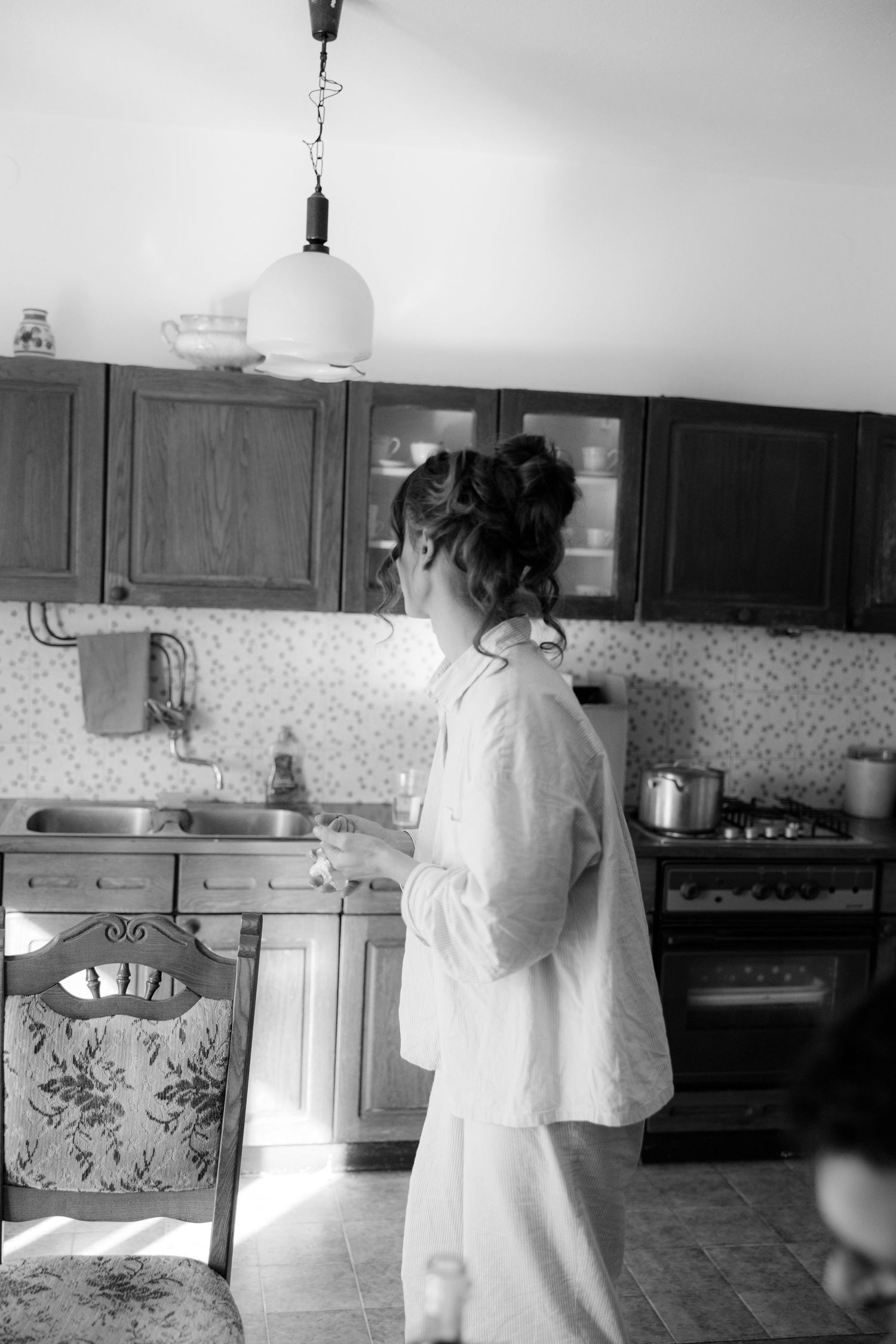 Black and white sequence showing someone in a white outfit moving through a vintage kitchen interior.