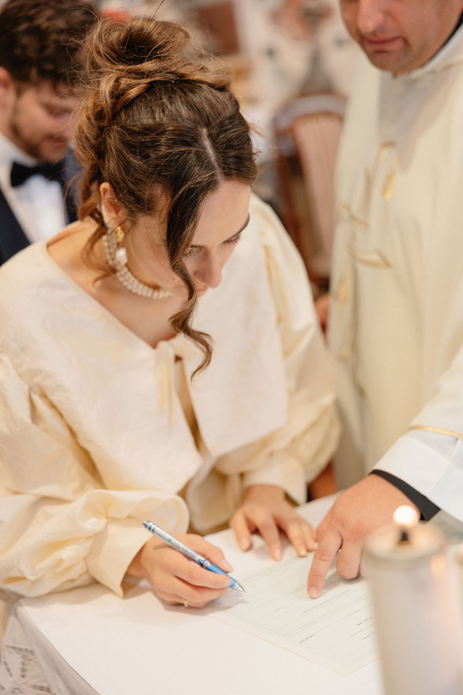Someone in cream-colored attire signing documents at a formal event.