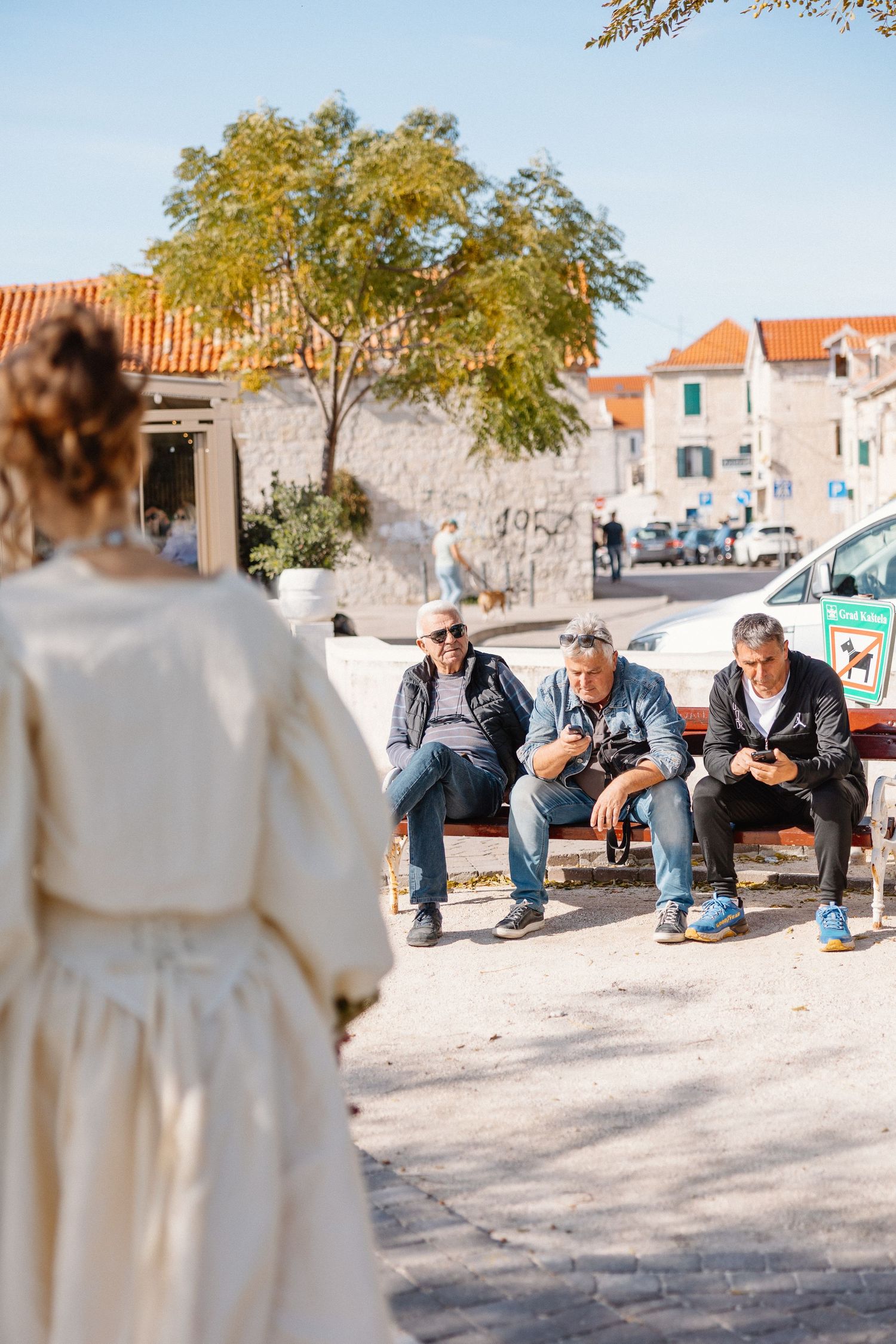 A group sits on a stone wall in a Mediterranean village setting with white buildings and terracotta roofs.