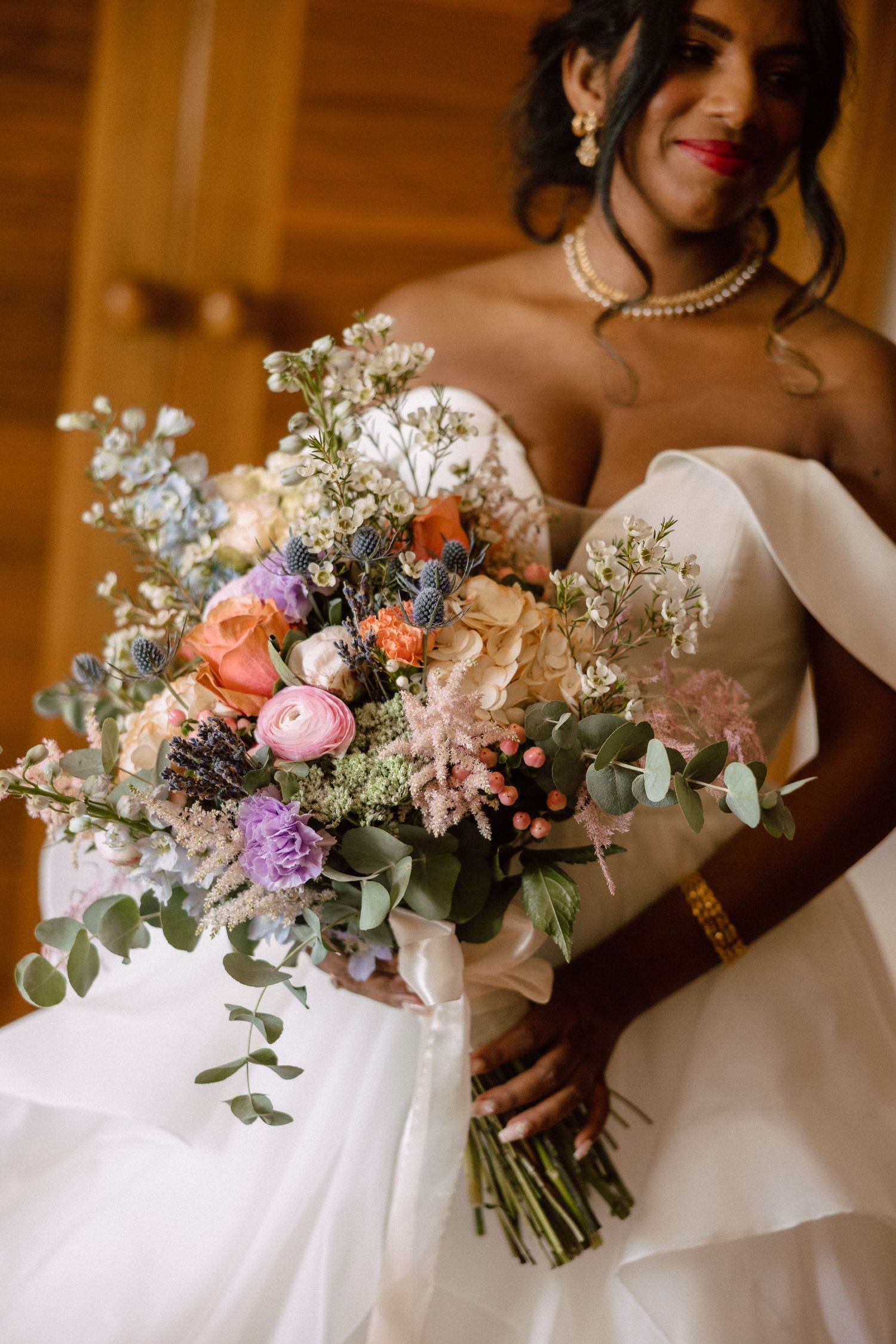 Bride in white strapless gown holding lush colorful wedding bouquet with ranunculus and eucalyptus.