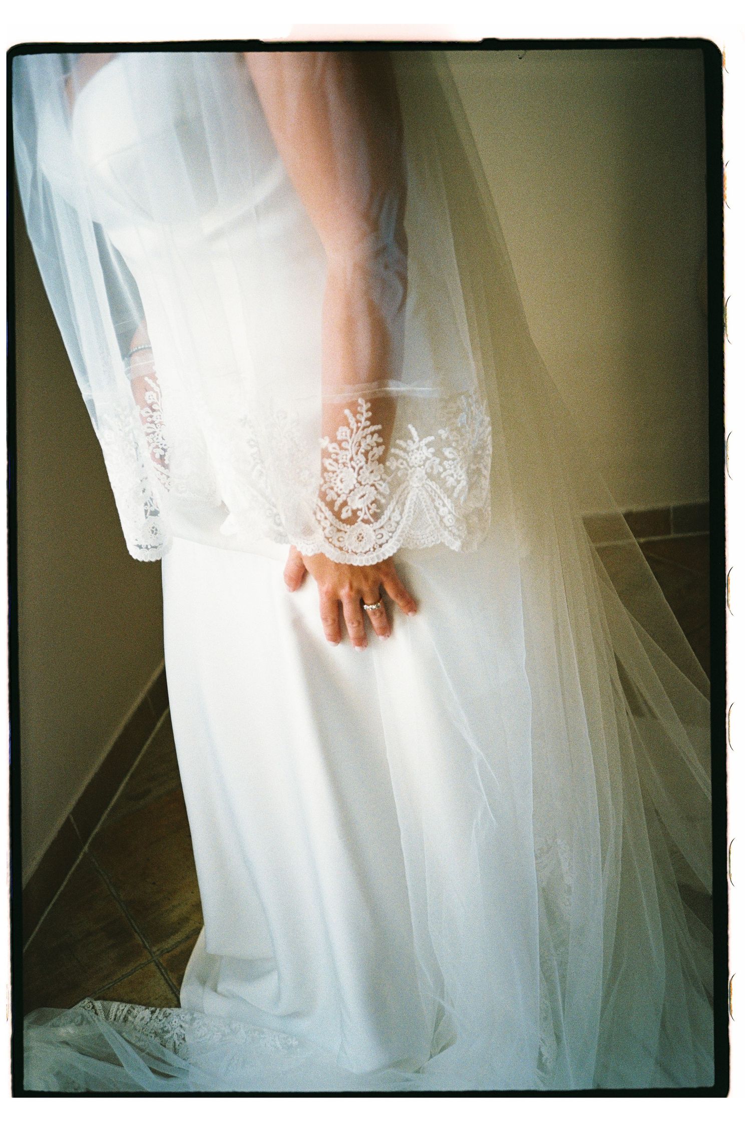 Bride in white lace wedding gown with veil, showcasing elegant lace cuff detail and diamond engagement ring.
