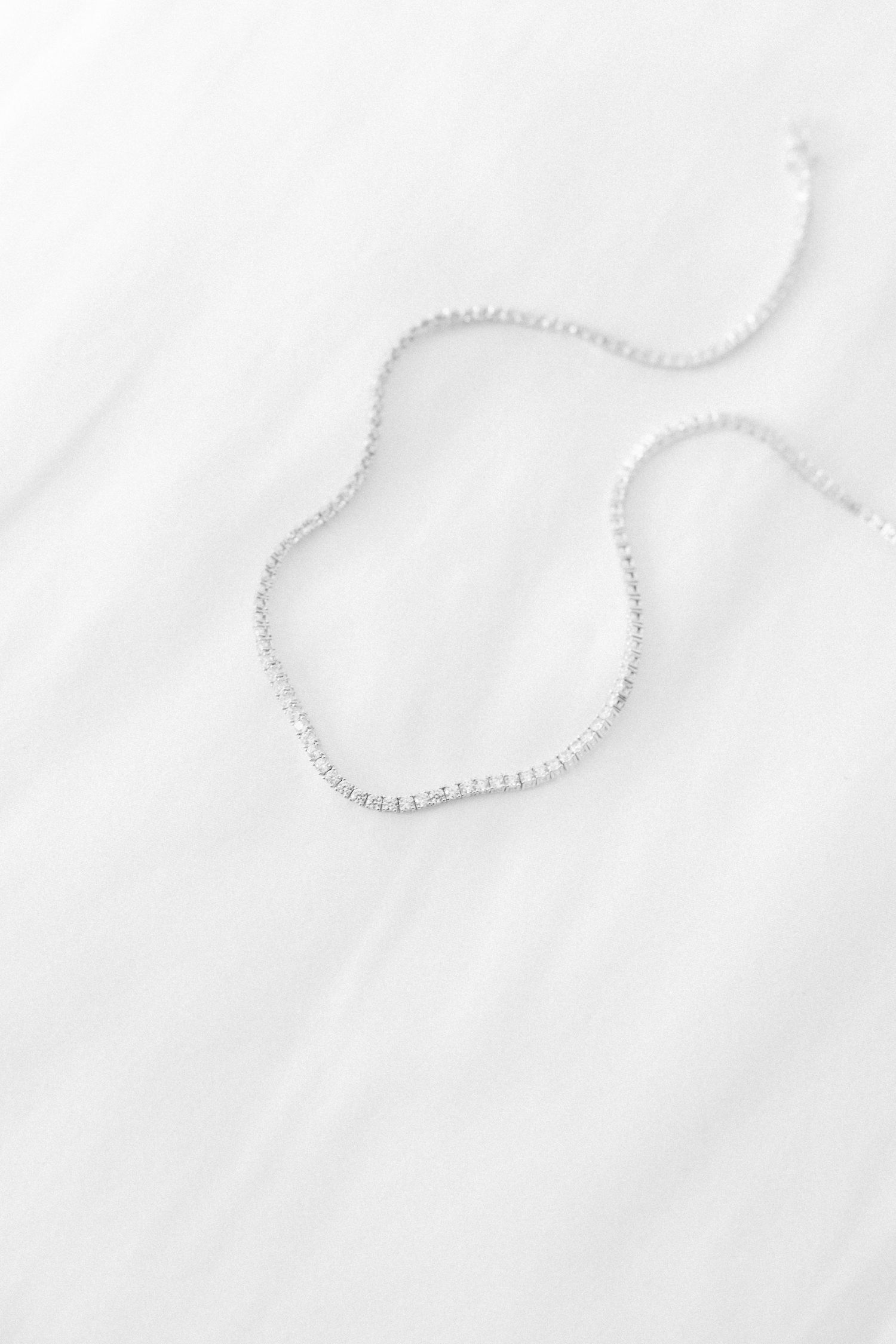 Delicate pearl necklace arranged in heart shape on white surface.