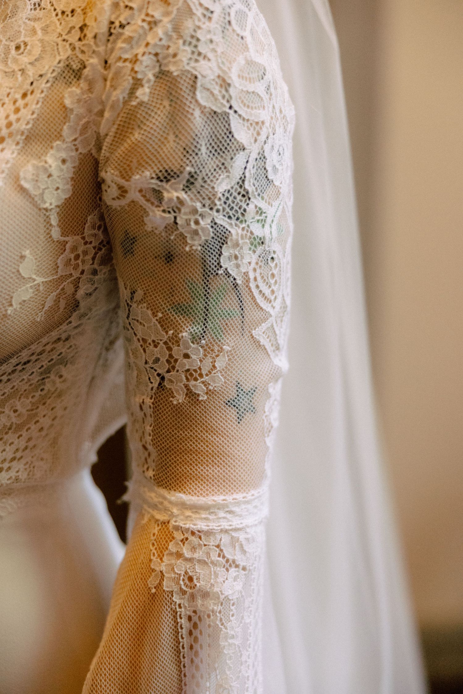 Close-up detail of delicate white lace wedding dress sleeve with intricate floral patterns and sheer fabric.