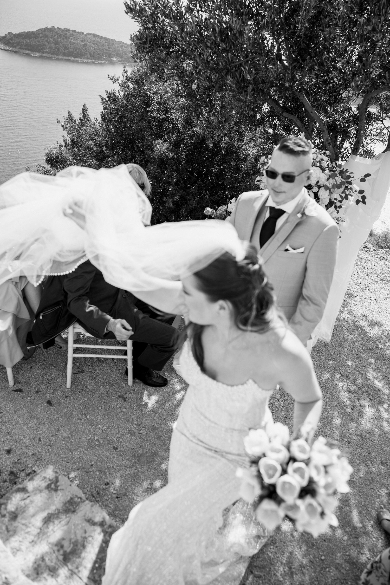 A wedding dress and veil blow gracefully in the breeze against a coastal backdrop.