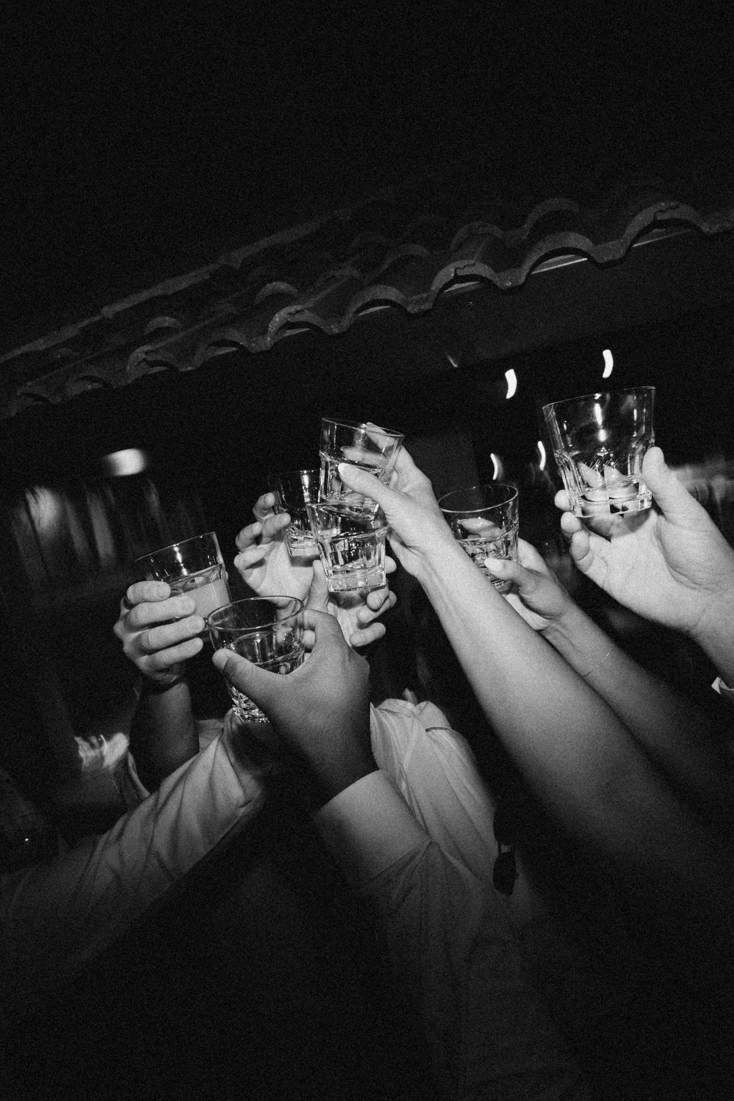 A line of raised glasses during a wedding toast captured in dramatic black and white.