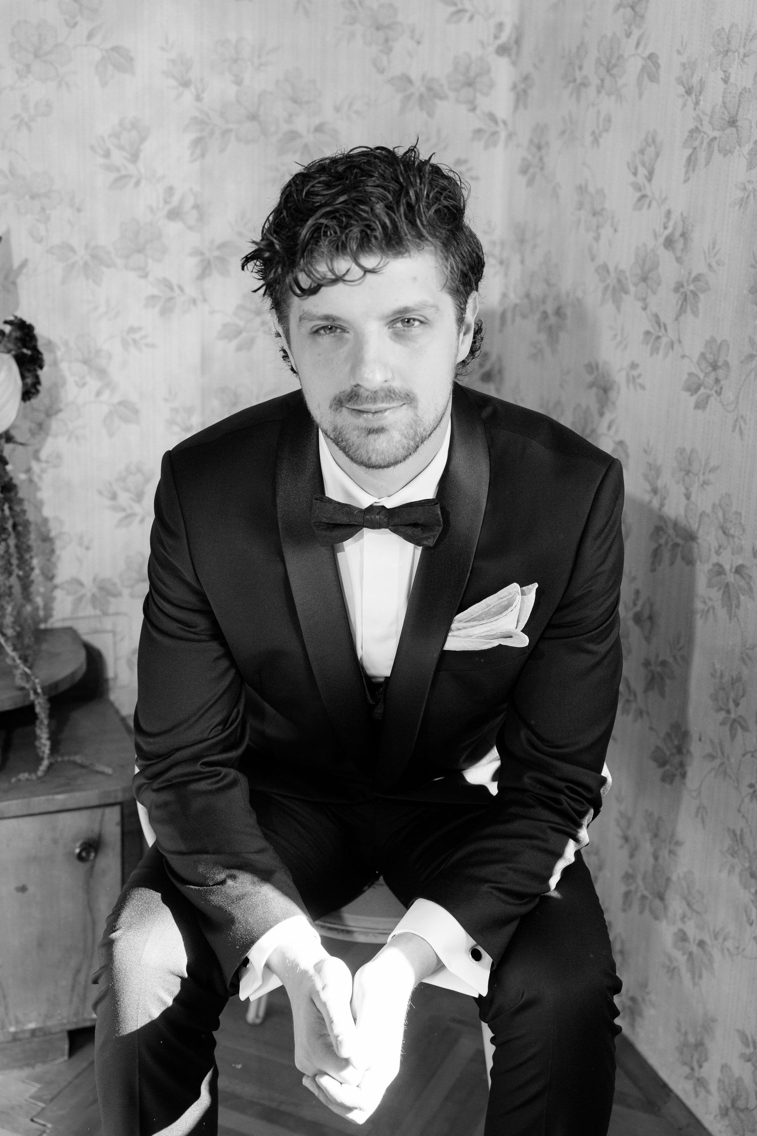 Black and white sequence of a groom in a tuxedo sitting and adjusting his bowtie.
