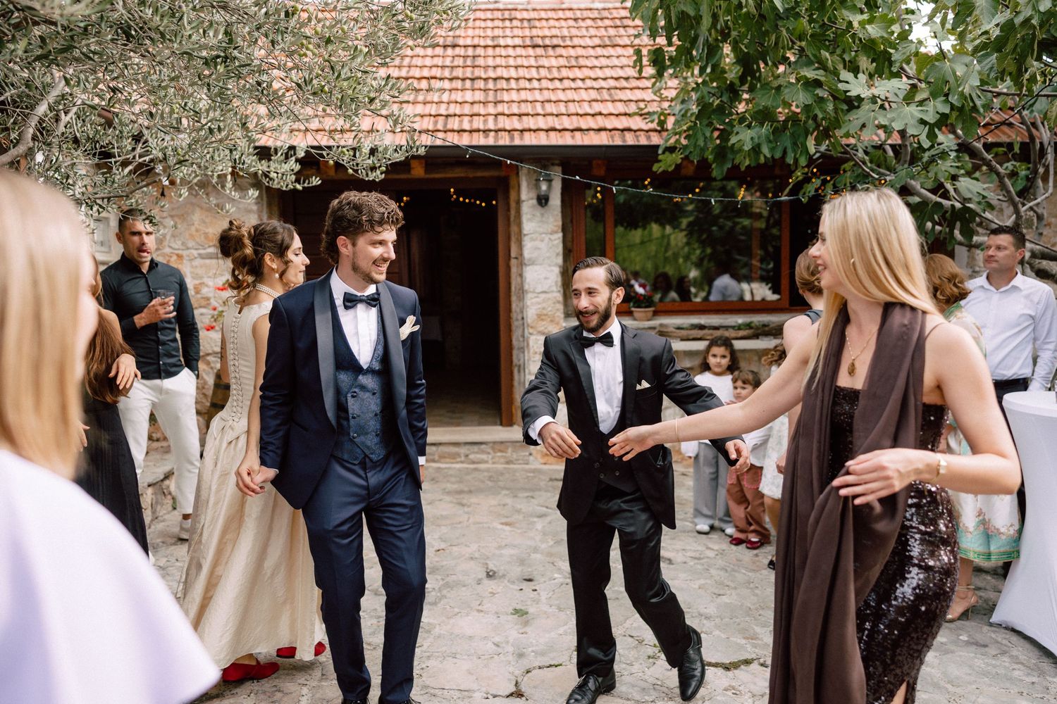 Wedding guests mingling outdoors at a rustic venue with terracotta roof tiles.