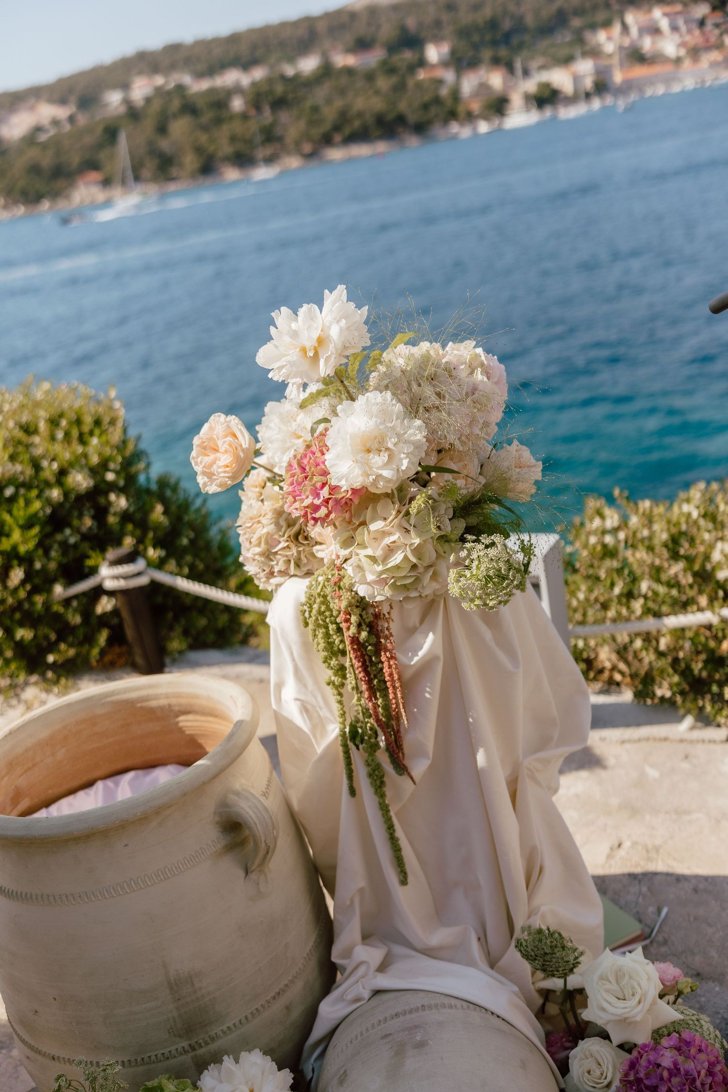 Elegant wedding bouquet with white peonies and pink hydrangeas displayed on stone terrace overlooking blue Adriatic Sea.