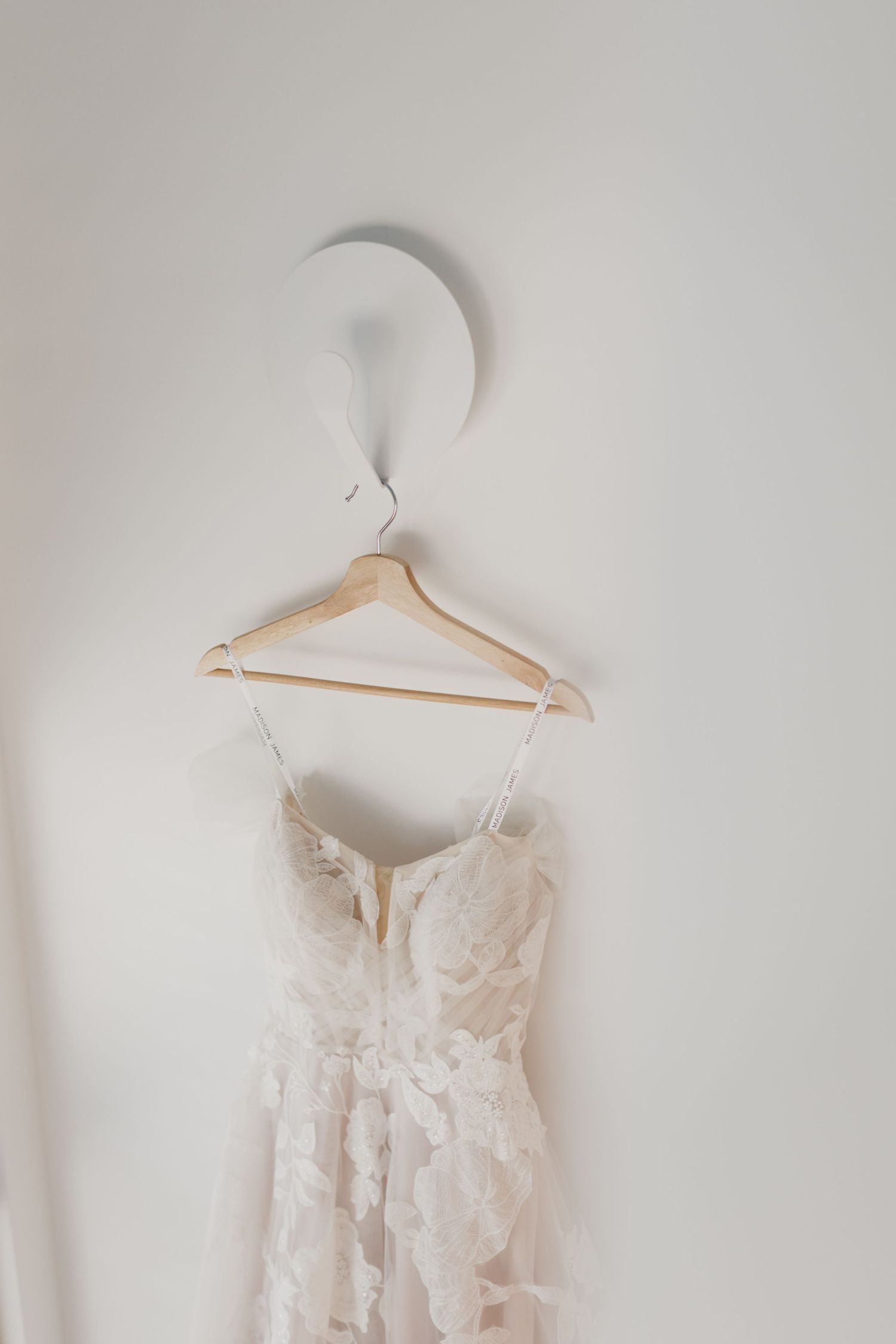 Delicate floral lace details on white wedding dress displayed on hanger.
