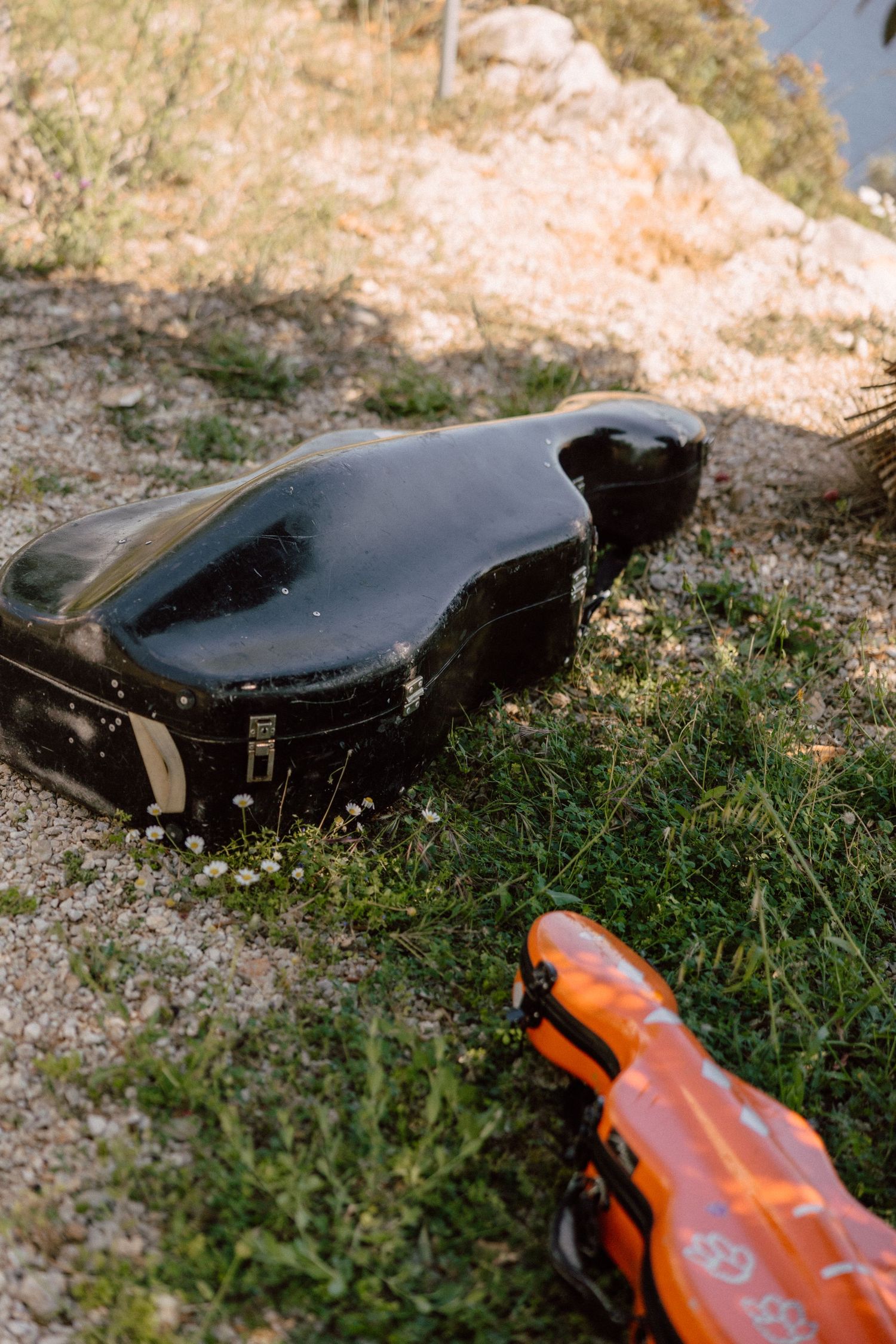Black violin case and orange accessory lying on grass outdoors.