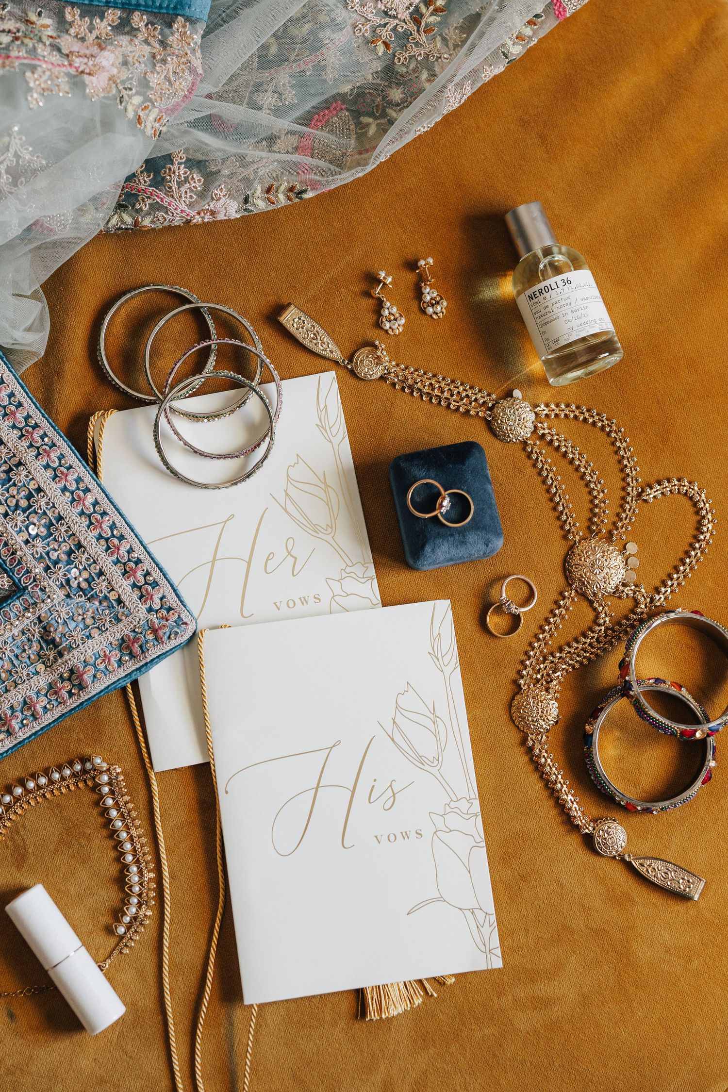 Wedding details including rings, pearls, invitations, and jewelry arranged on brown leather and floral fabric surfaces.