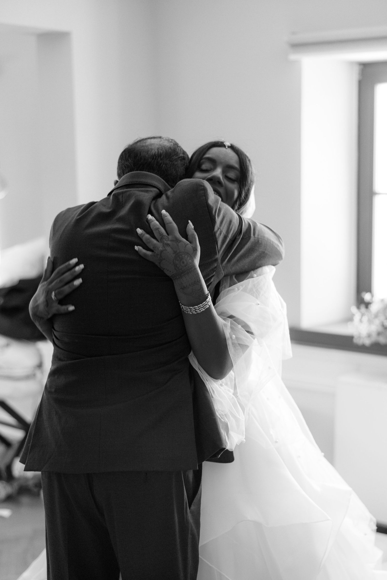 Emotional black and white photo of a bride in a white gown sharing a heartfelt hug with her father.