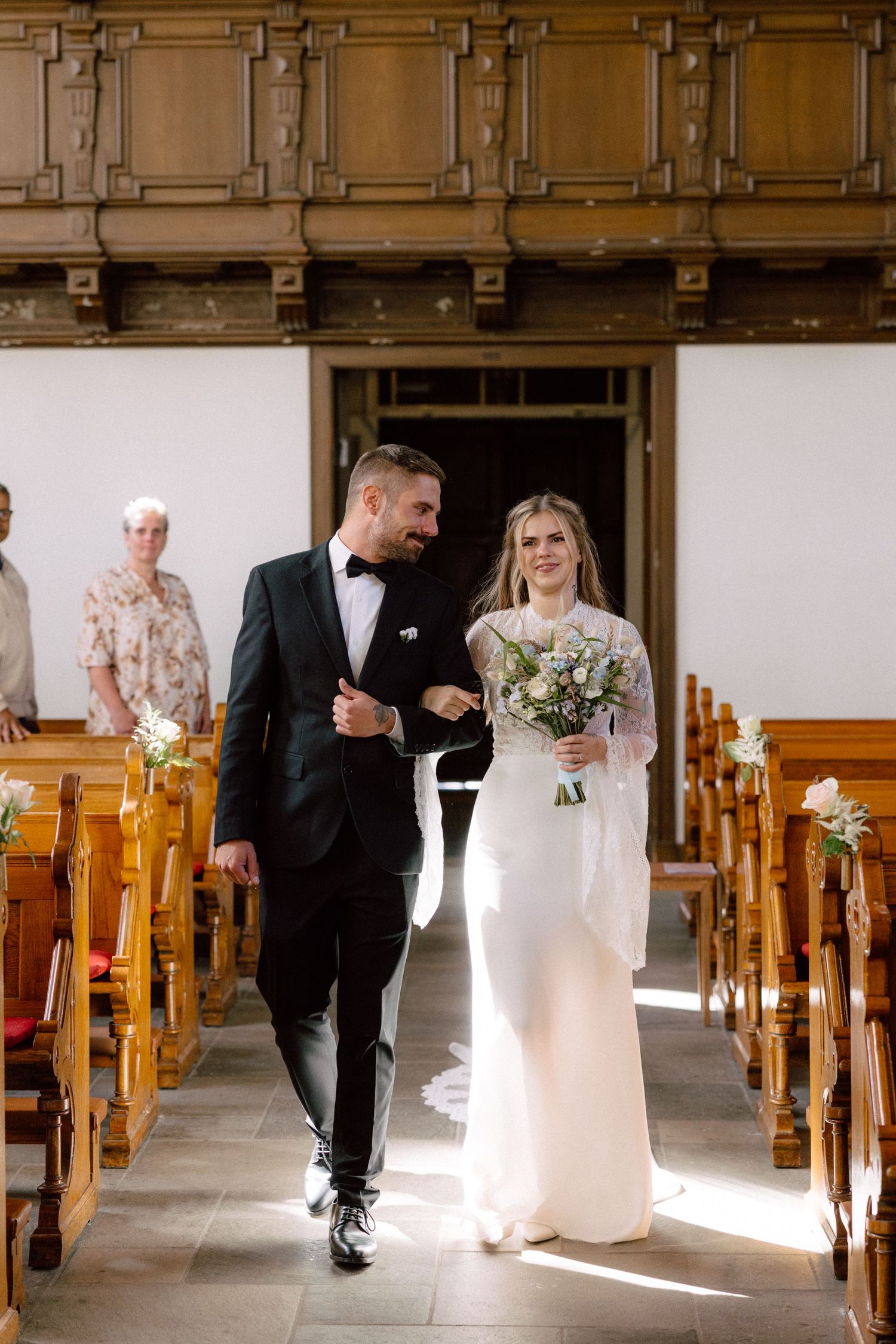 Sun-lit church aisle with wooden pews during wedding processional.