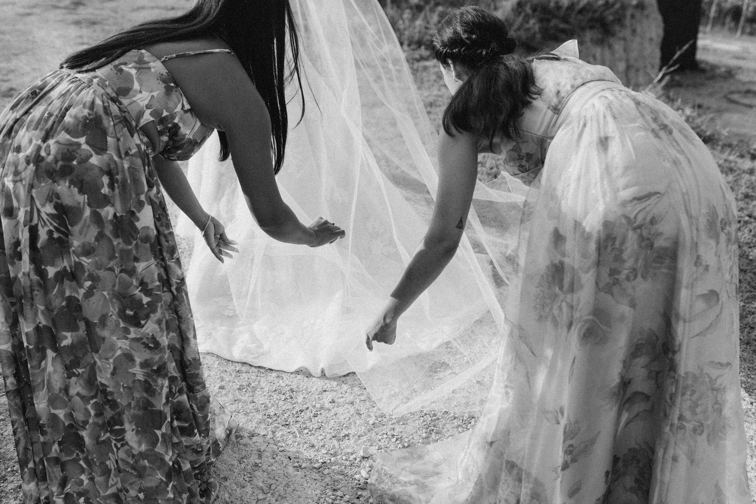Wedding party in floral dresses helping with bridal gown outdoors.
