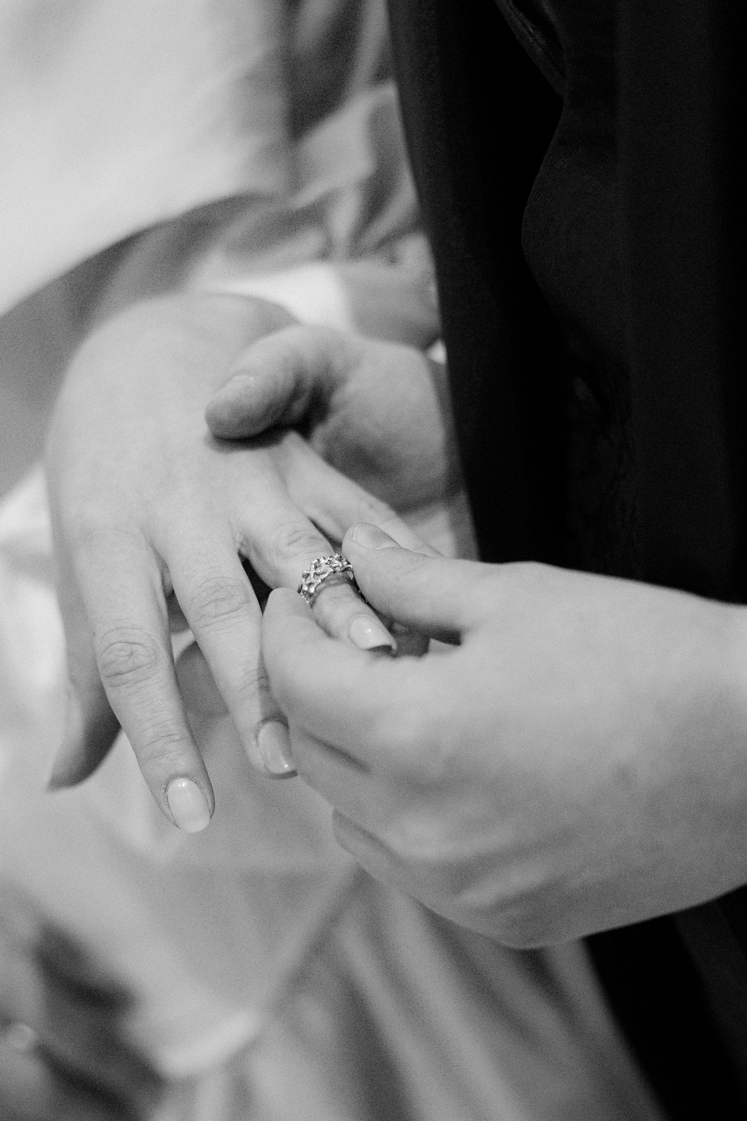 Close-up black and white shot of hands exchanging rings during a ceremony.