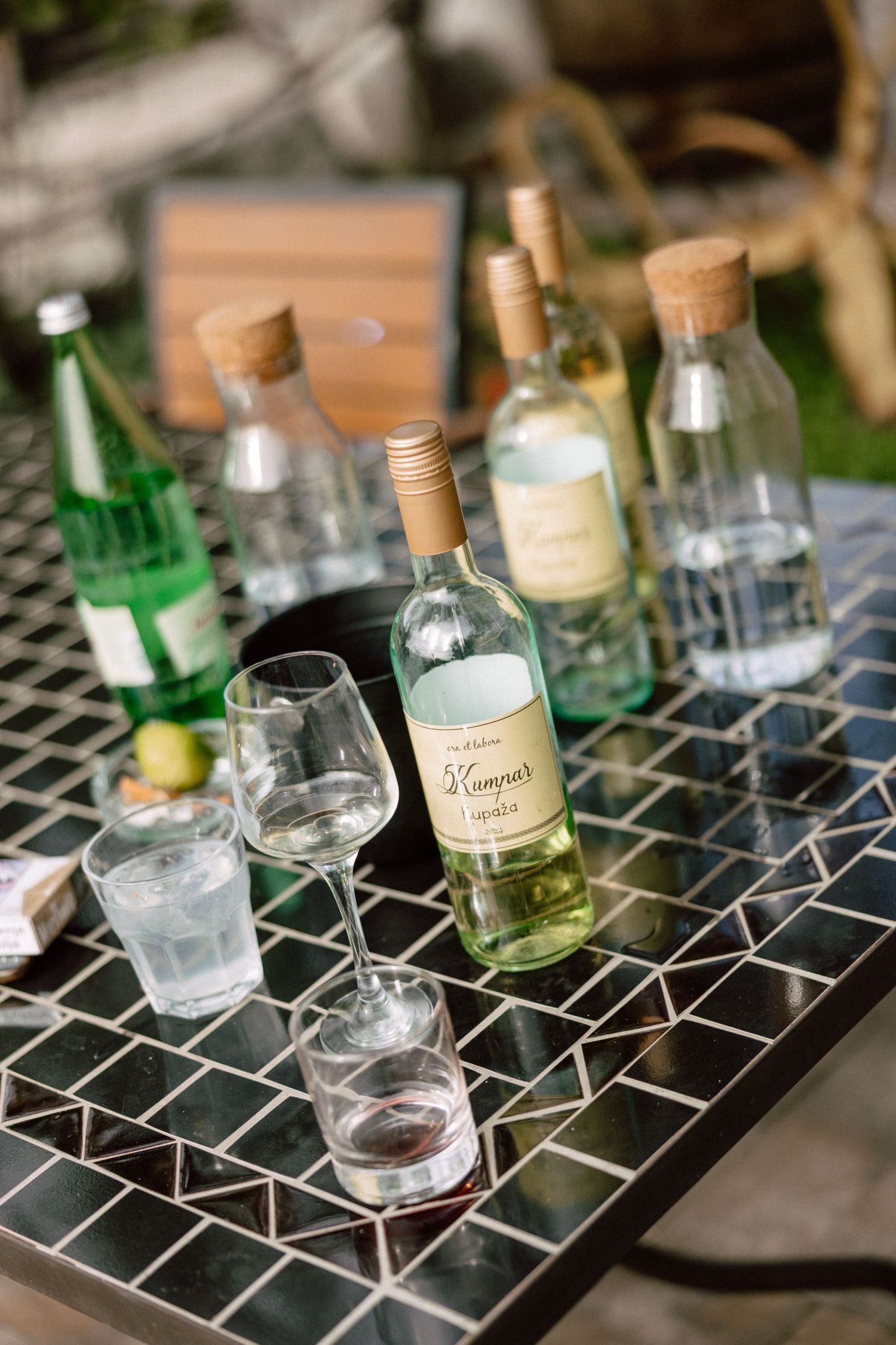 Various glass bottles and cocktail glasses arranged on a geometric patterned surface at a wedding bar setup.
