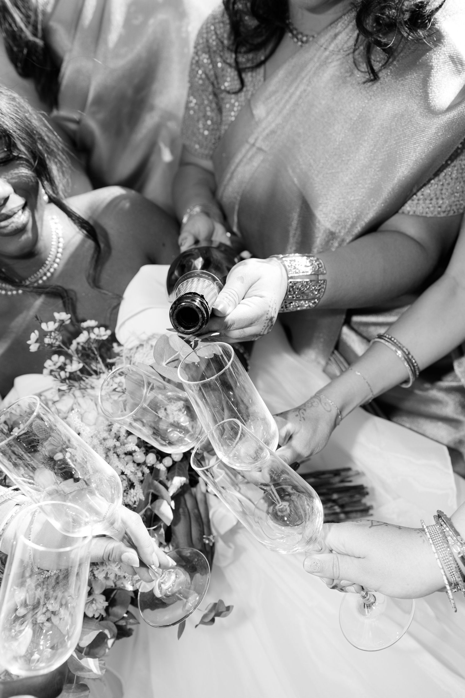 Wedding guests pour champagne into glasses near bridal bouquet in black and white celebration photo.