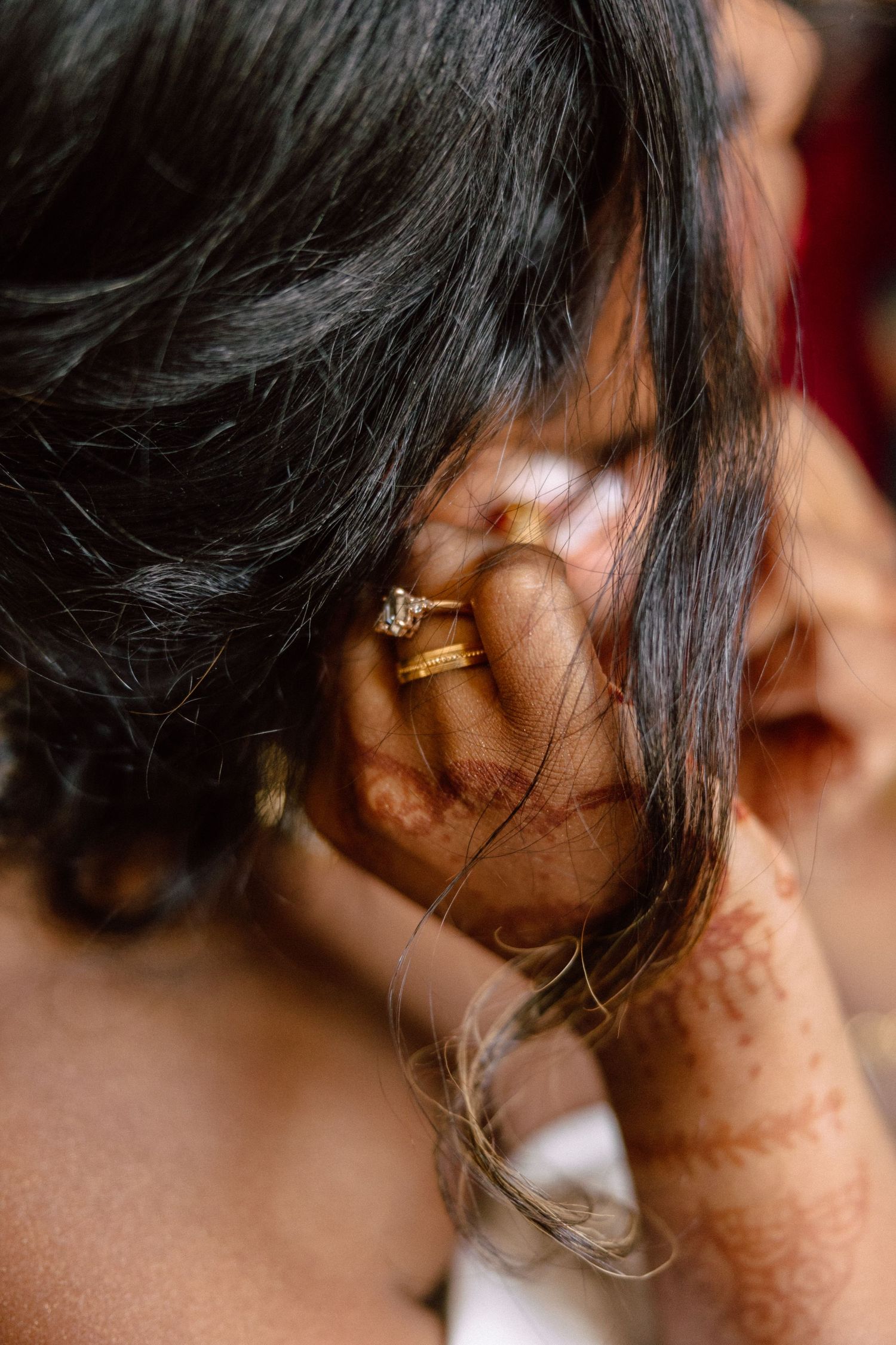 Close-up of bride with henna-adorned hand placing a gold diamond earring, dark hair falling softly.