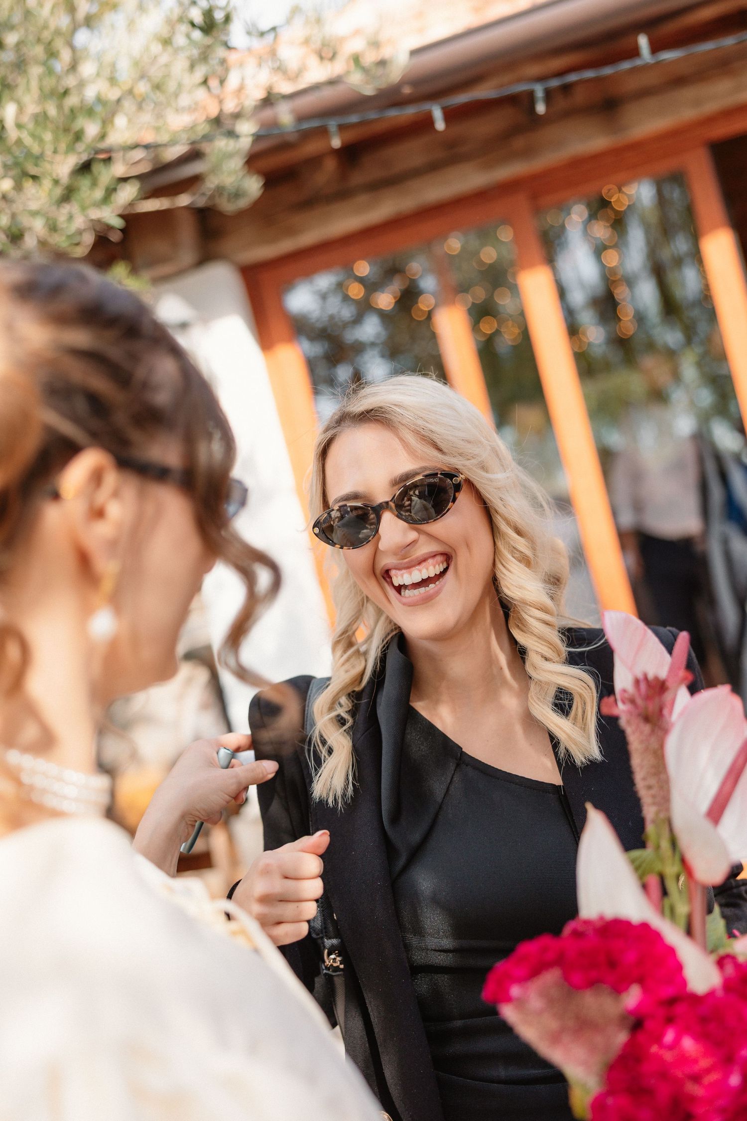 People enjoying conversation at an outdoor gathering under a wooden pergola with bright flowers.