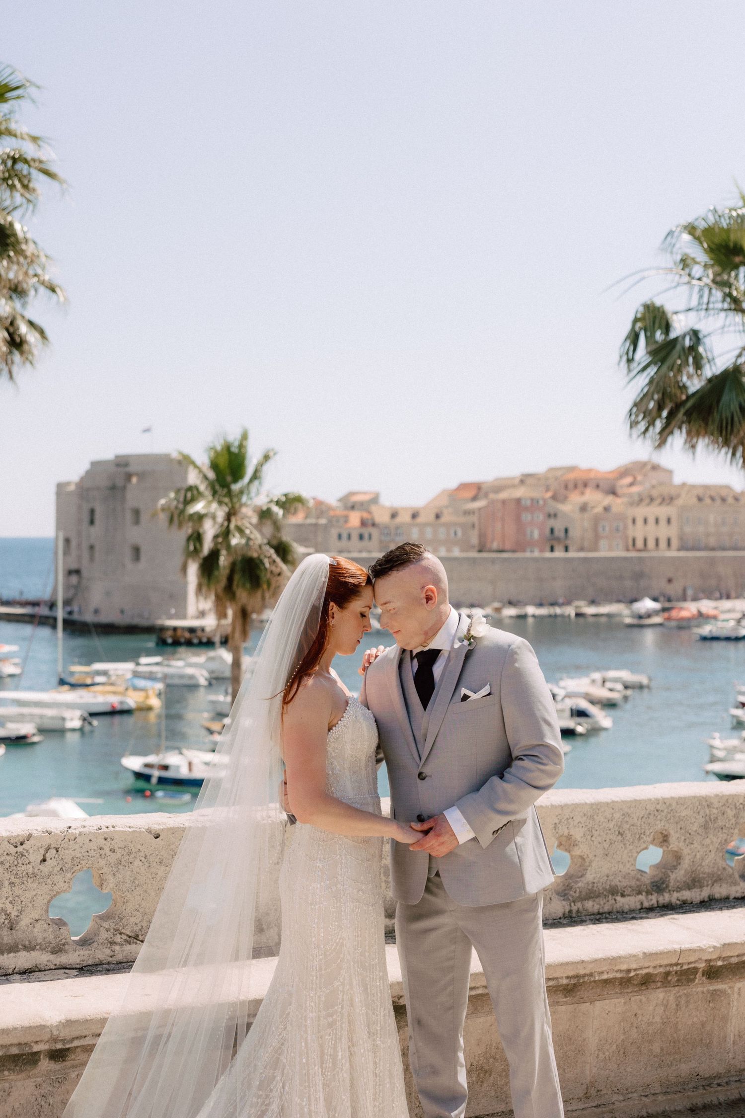 A romantic wedding couple share intimate moments along the waterfront of Dubrovnik, Croatia with boats and architecture in view.