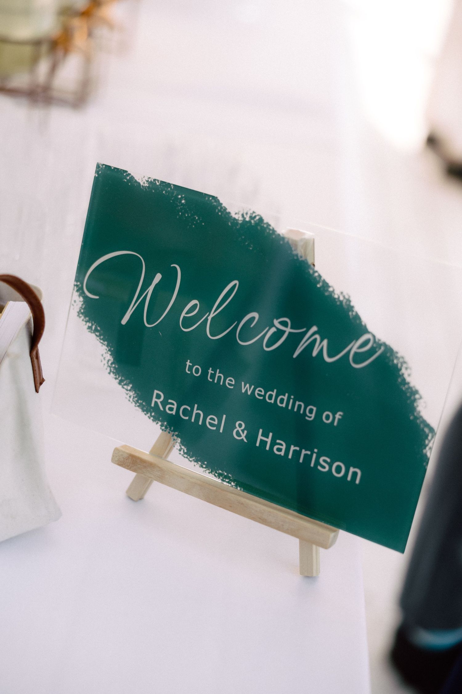Green acrylic welcome wedding sign reading Rachel and Harrison on wooden easel.