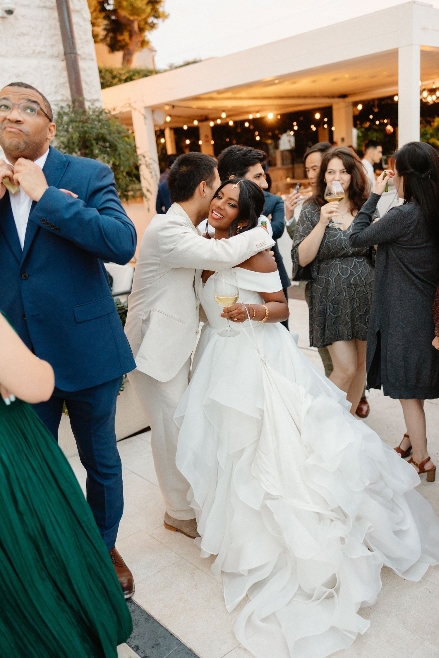 Bride in ruffled white gown laughs while dancing with groom at outdoor reception.