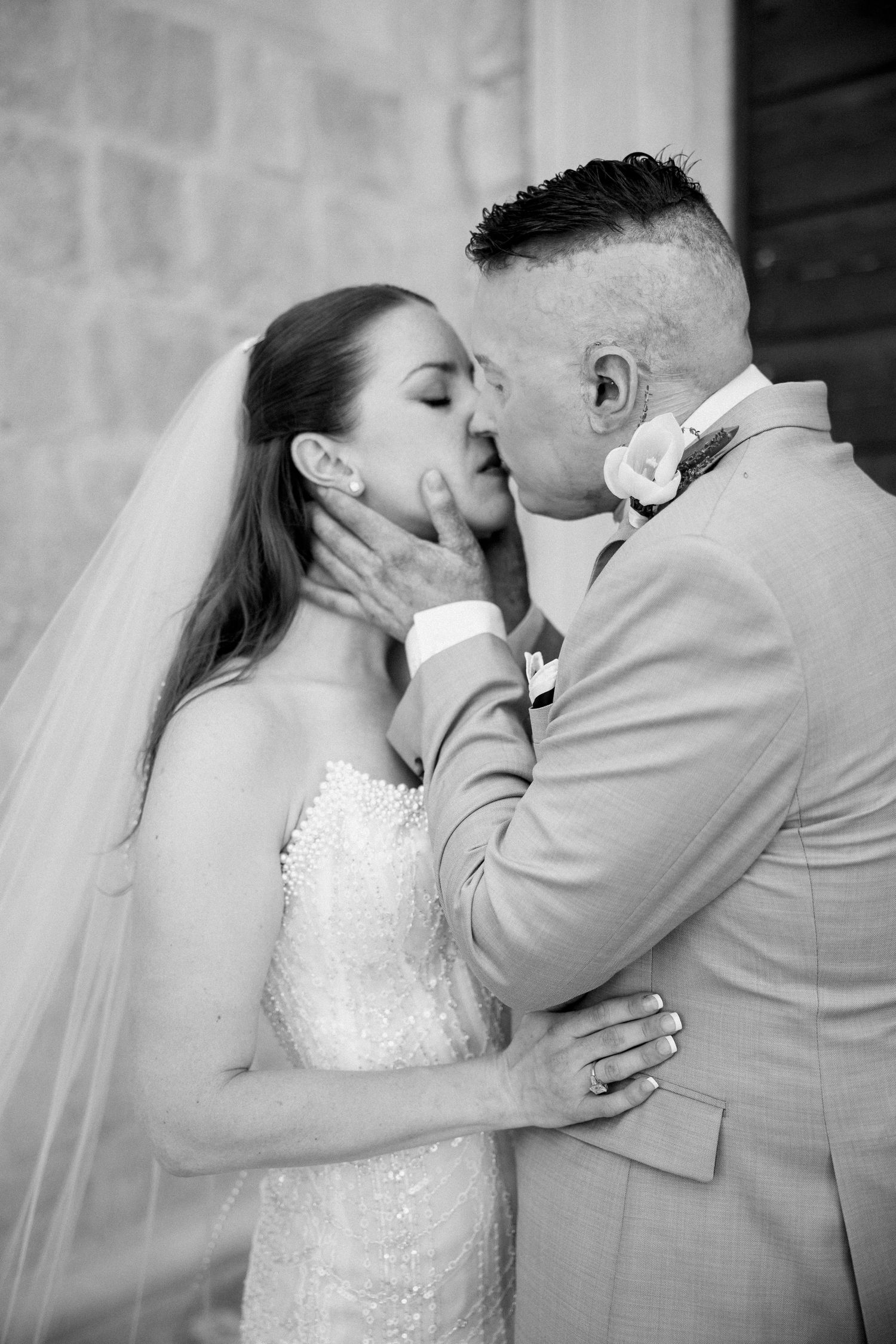 Intimate wedding moment captured in black and white against a stone wall backdrop.