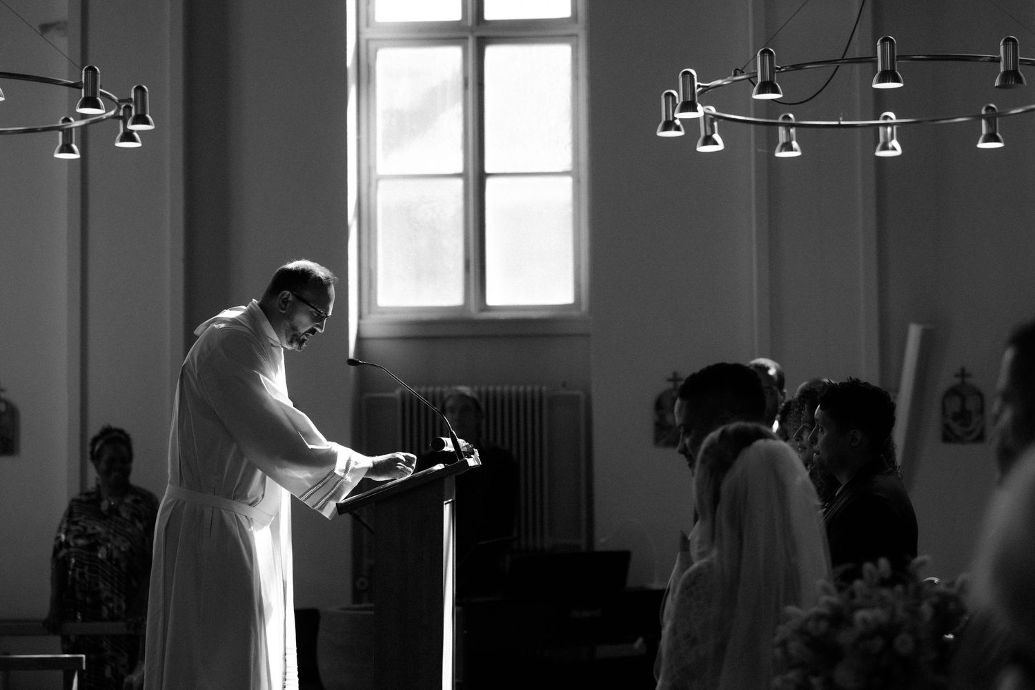 Dramatic silhouette of church interior with hanging light fixtures and windows.