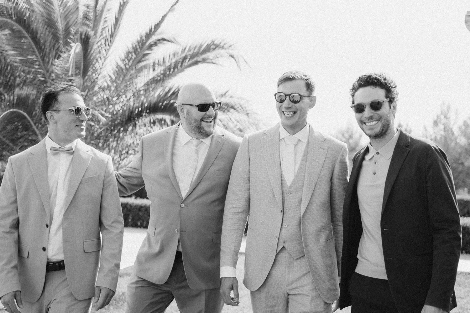 Black and white photo of four groomsmen posing together by palm trees.