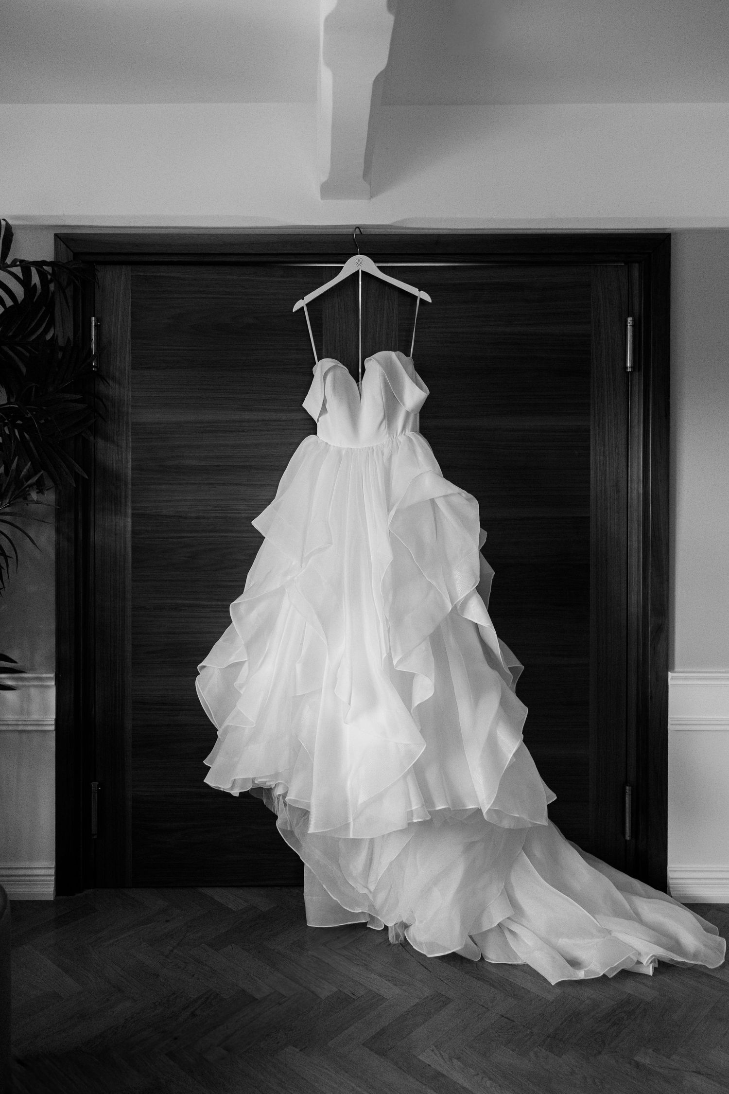 Elegant strapless ball gown wedding dress with ruffled skirt and train hanging on a door in black and white.