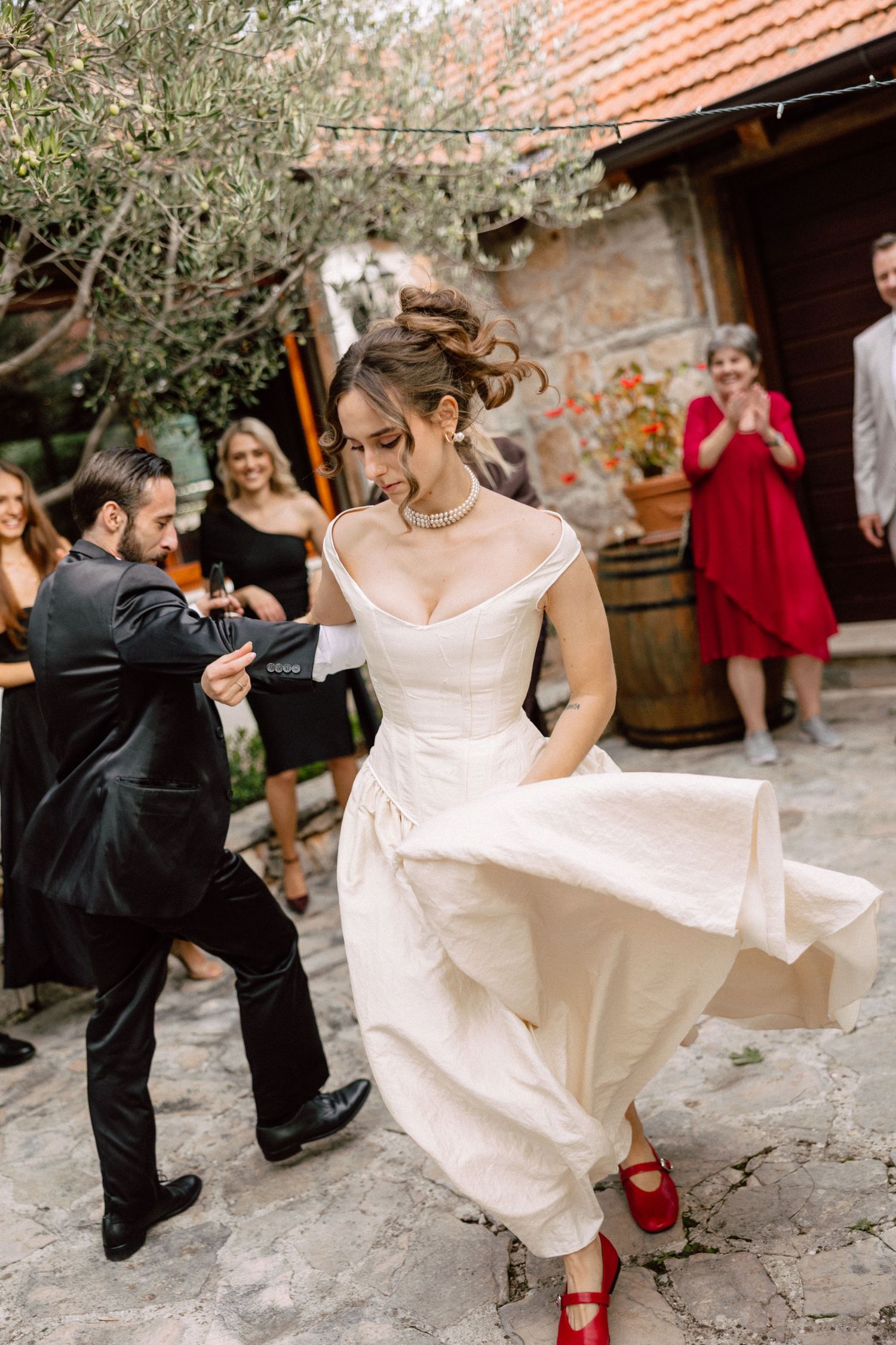 Bride in white dress with red shoes dancing at outdoor wedding celebration.
