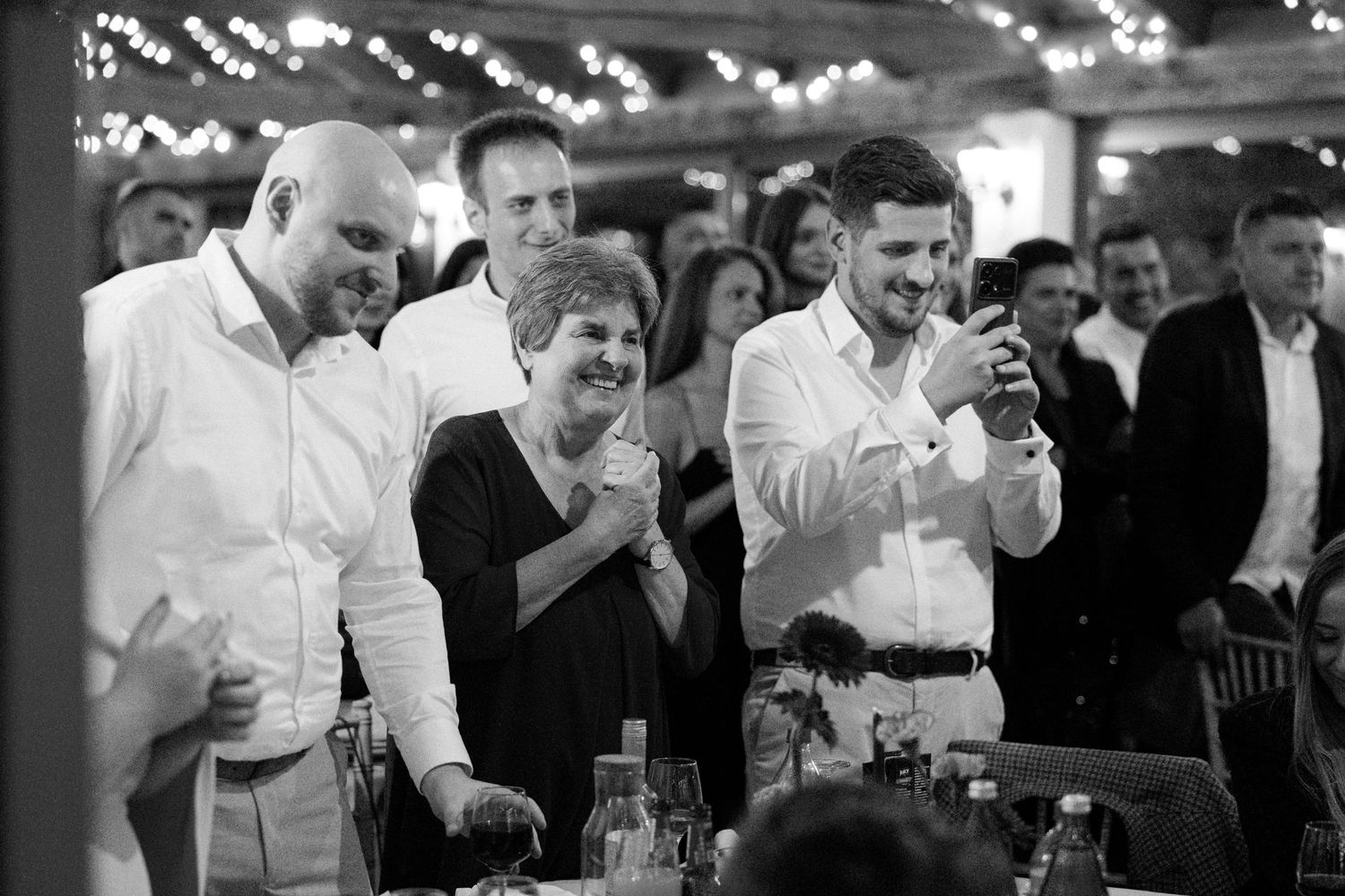 Black and white photo of wedding reception guests with bokeh lights in background.